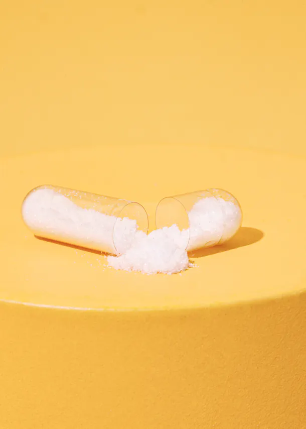 a clear capsule filled with white powder on a yellow surface