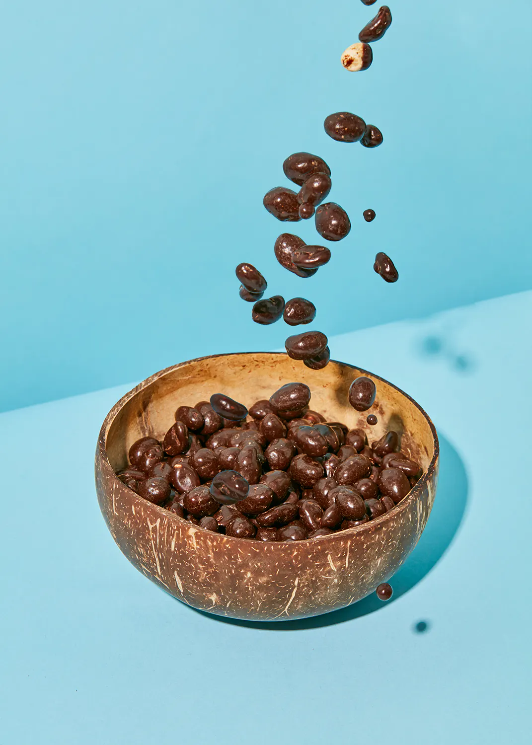 chocolate covered nuts falling into a bowl on a blue surface
