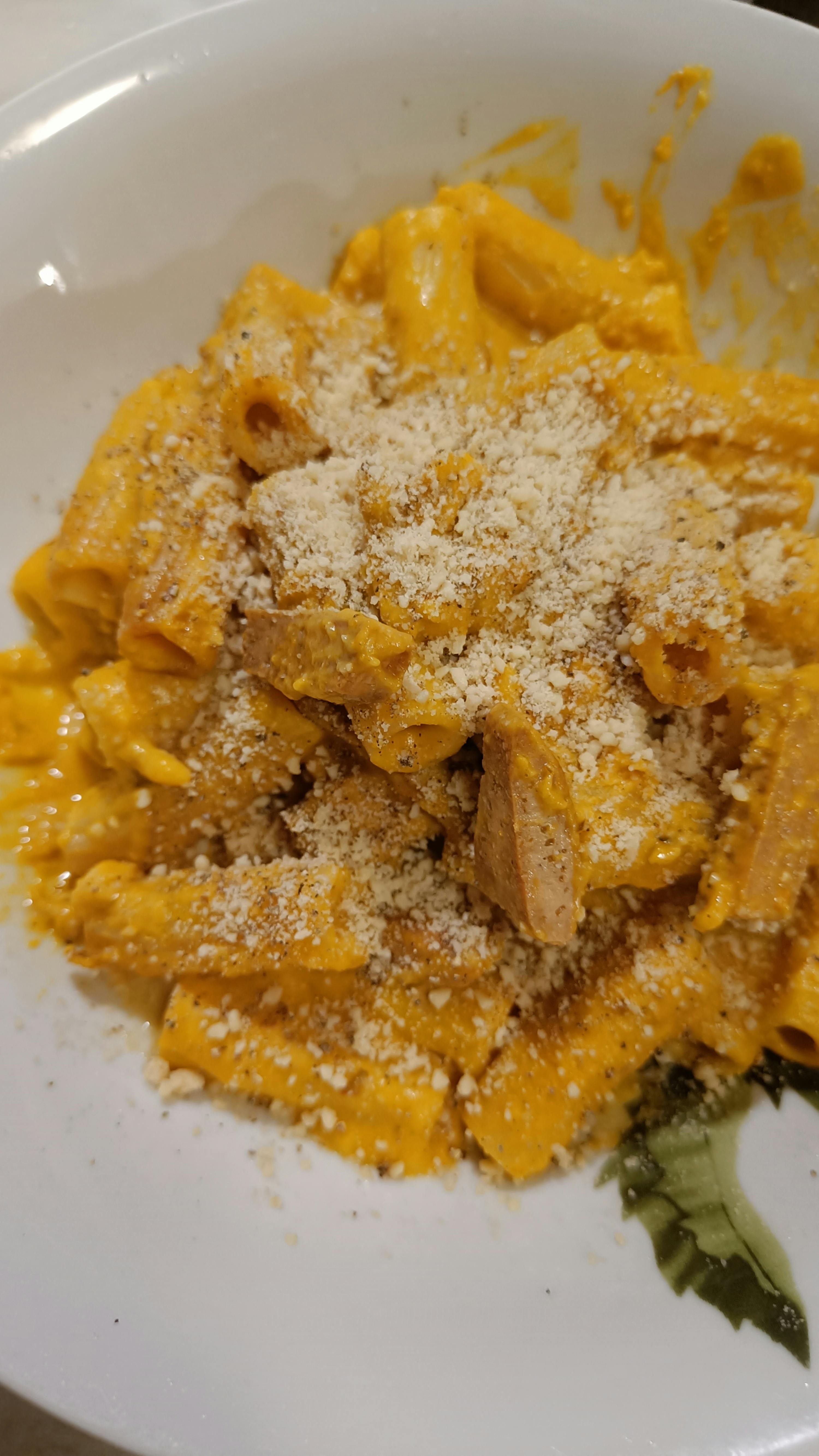 ein weißer Teller mit Nudeln und Käse auf einem Tisch