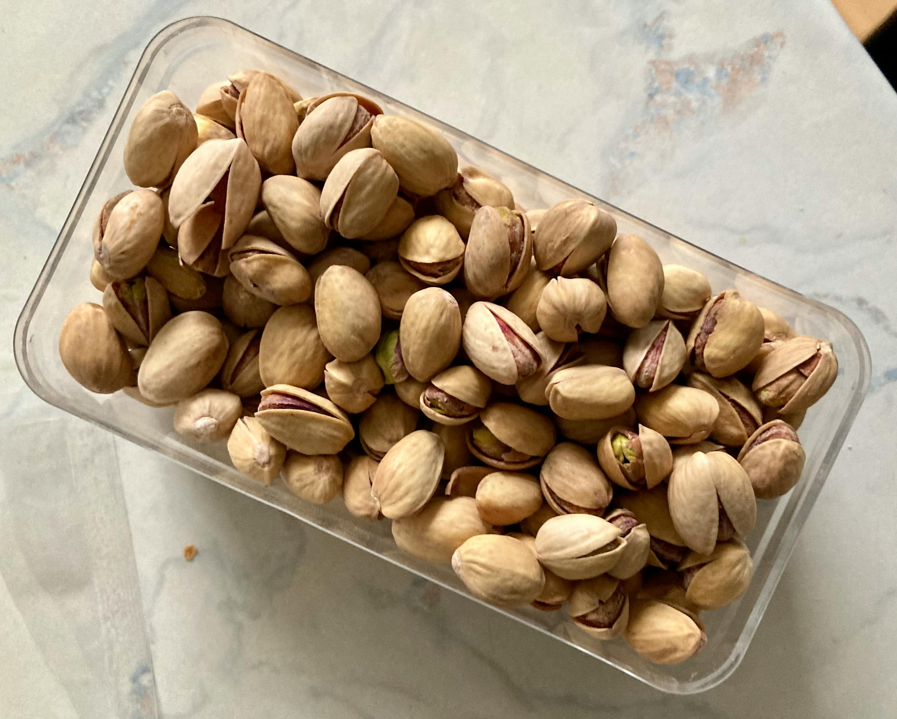 ein Plastikbehälter voller Pistazien liegt auf einem Tisch