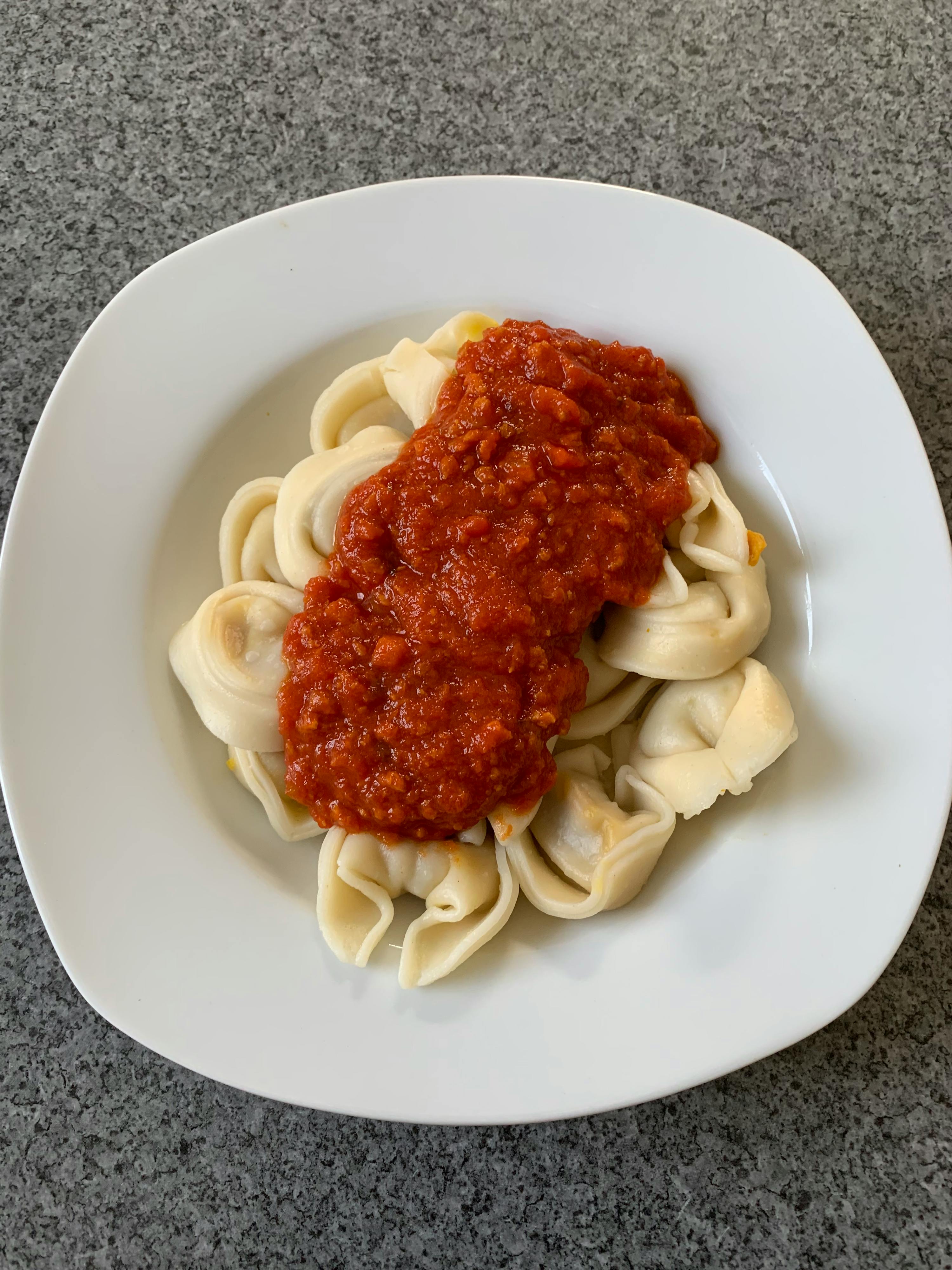 un piatto bianco con tortellini e salsa di pomodoro