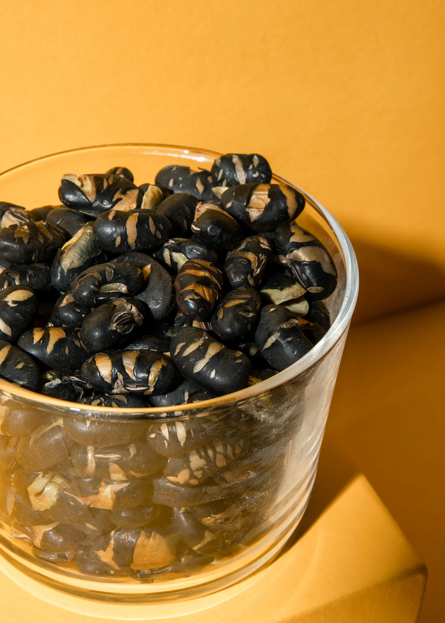 un bol en verre rempli de haricots noirs sur un fond jaune