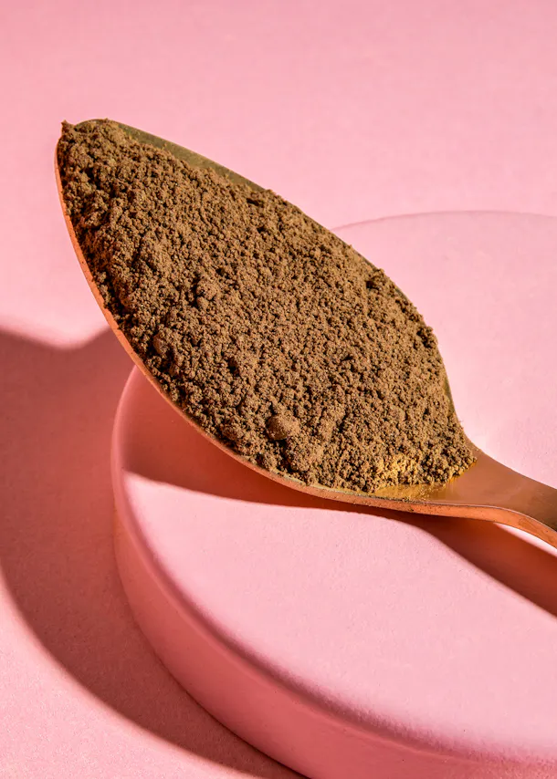 une cuillère remplie de poudre est posée sur un plateau rose