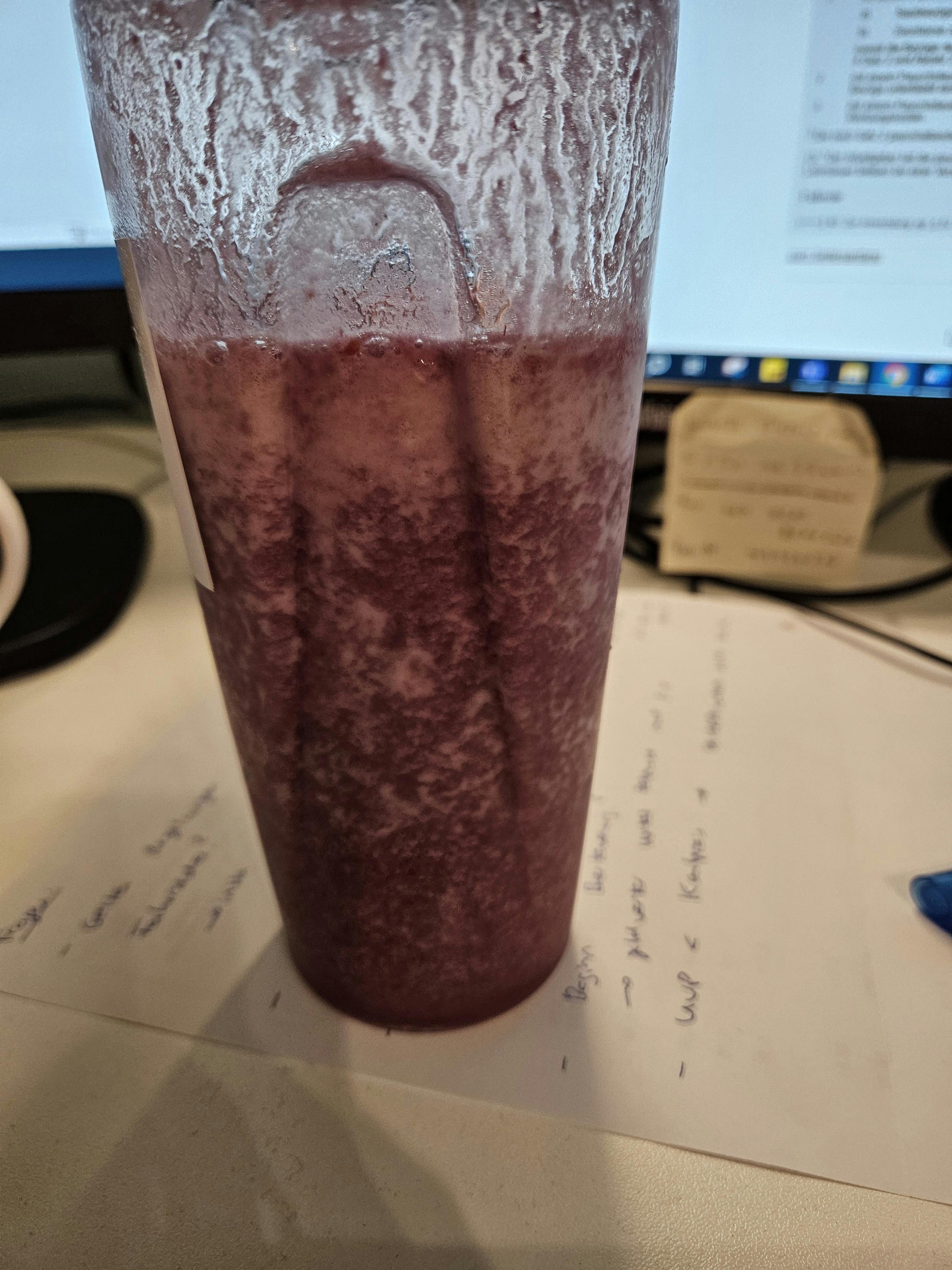 a cup of purple liquid sits on a desk in front of a computer screen