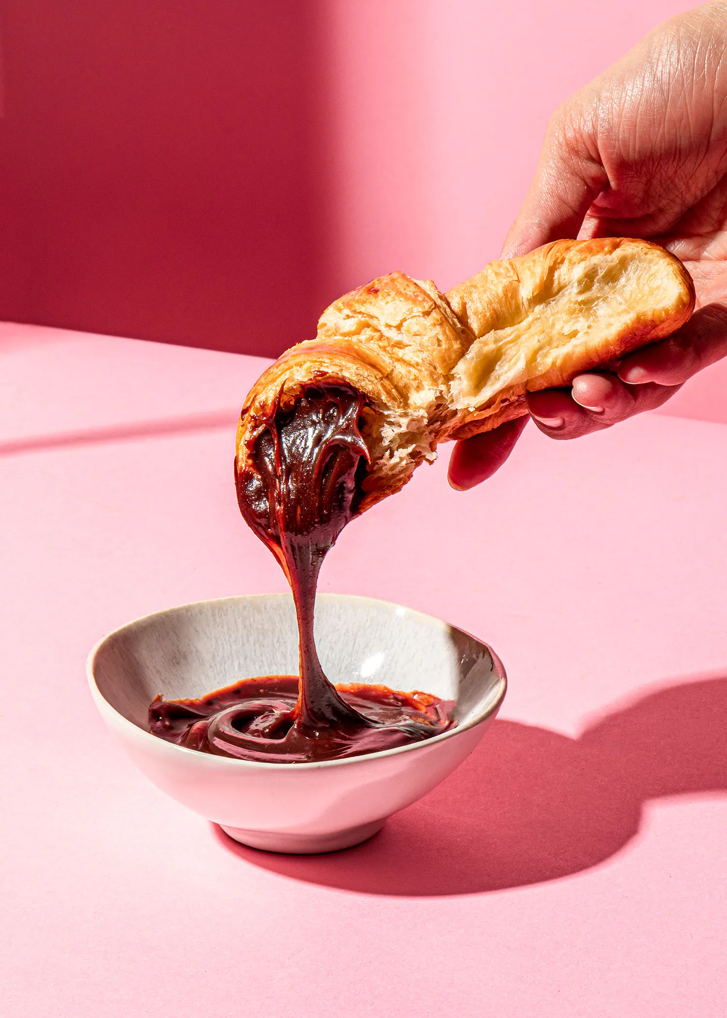 une personne verse du chocolat sur un croissant dans un bol