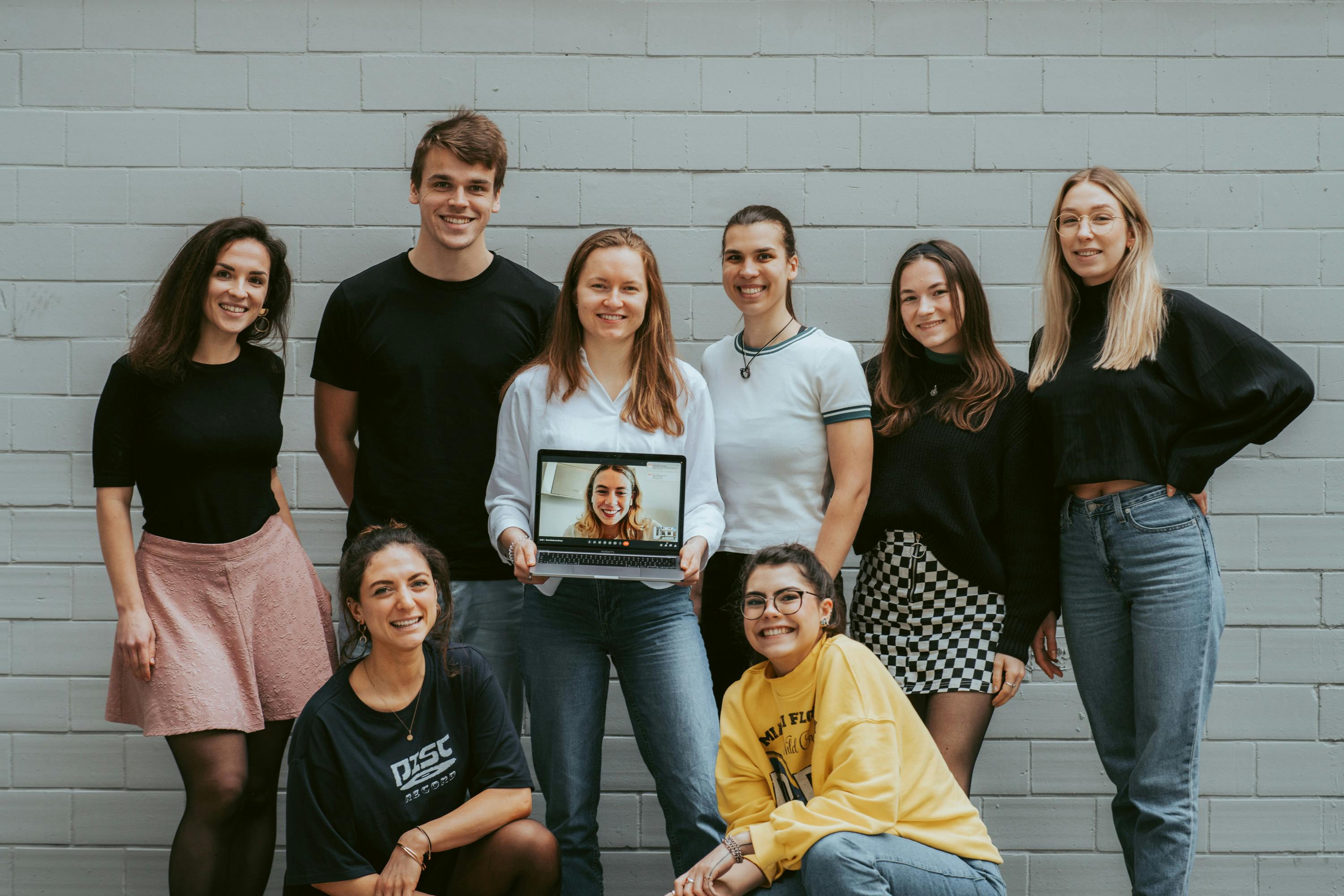 un gruppo di persone in piedi uno accanto all'altro con una donna che tiene in mano un computer portatile