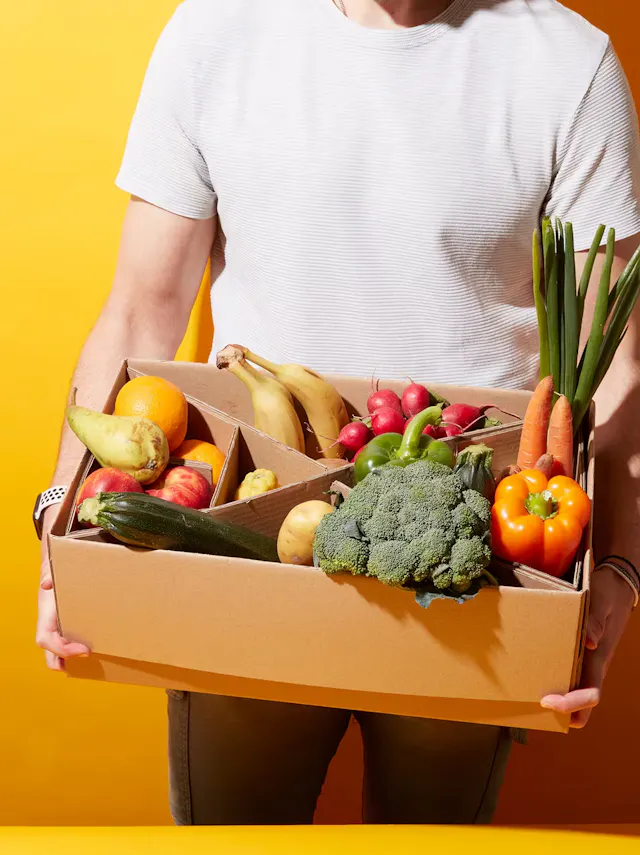 ein Mann hält eine Schachtel mit Obst und Gemüse in seinen Händen