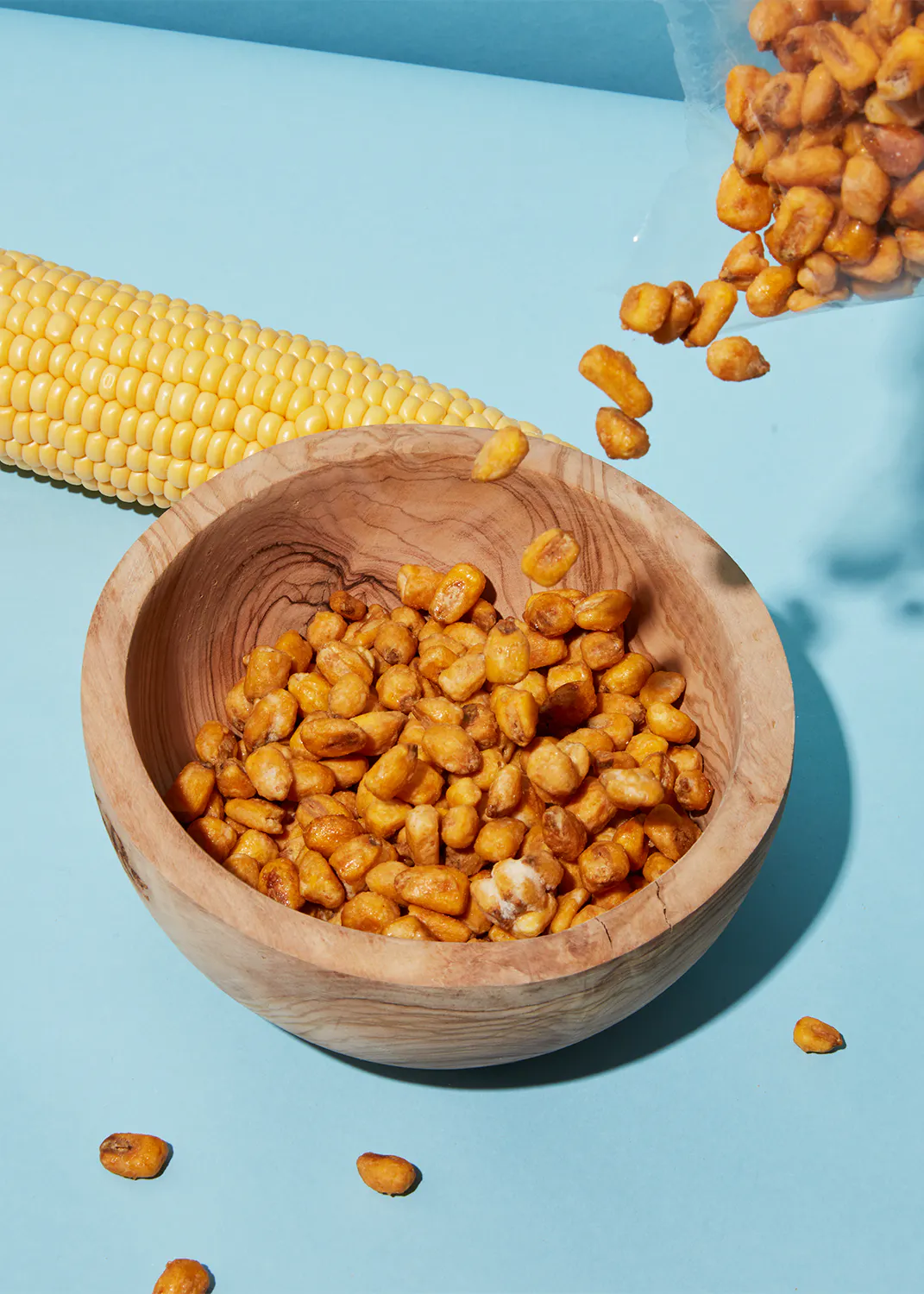 un bol en bois rempli de graines de maïs avec une épi de maïs en arrière-plan