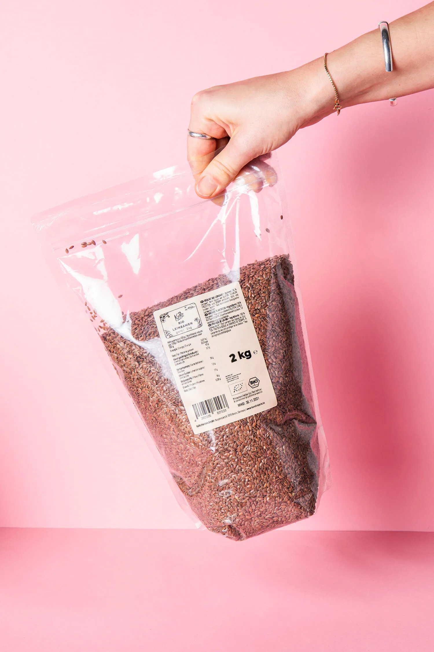 une personne tient un sac de 2 kg de graines sur fond rose