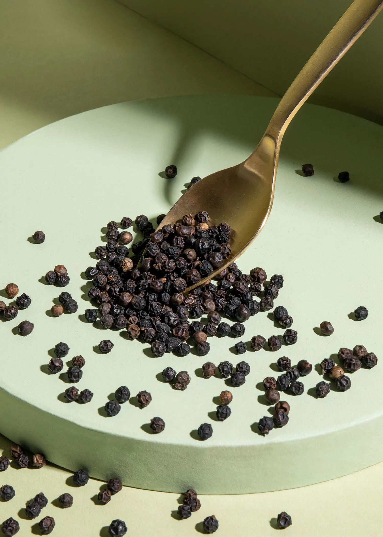 une cuillère remplie de poivre noir est posée sur une assiette verte