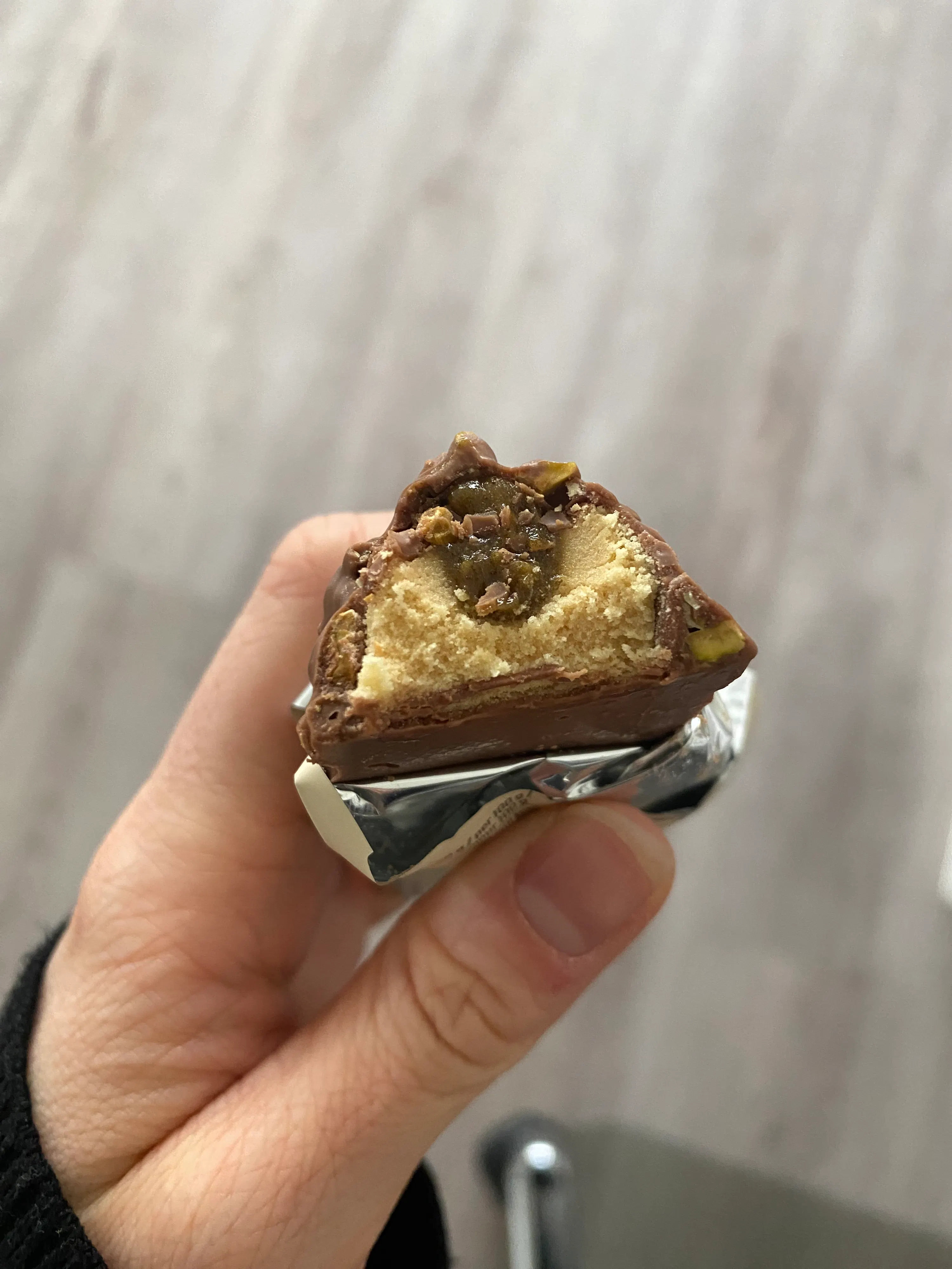 eine hand hält einen angebissenen schokoriegel, der eine helle füllung und eine dunkle, stückige schicht in der mitte zeigt.