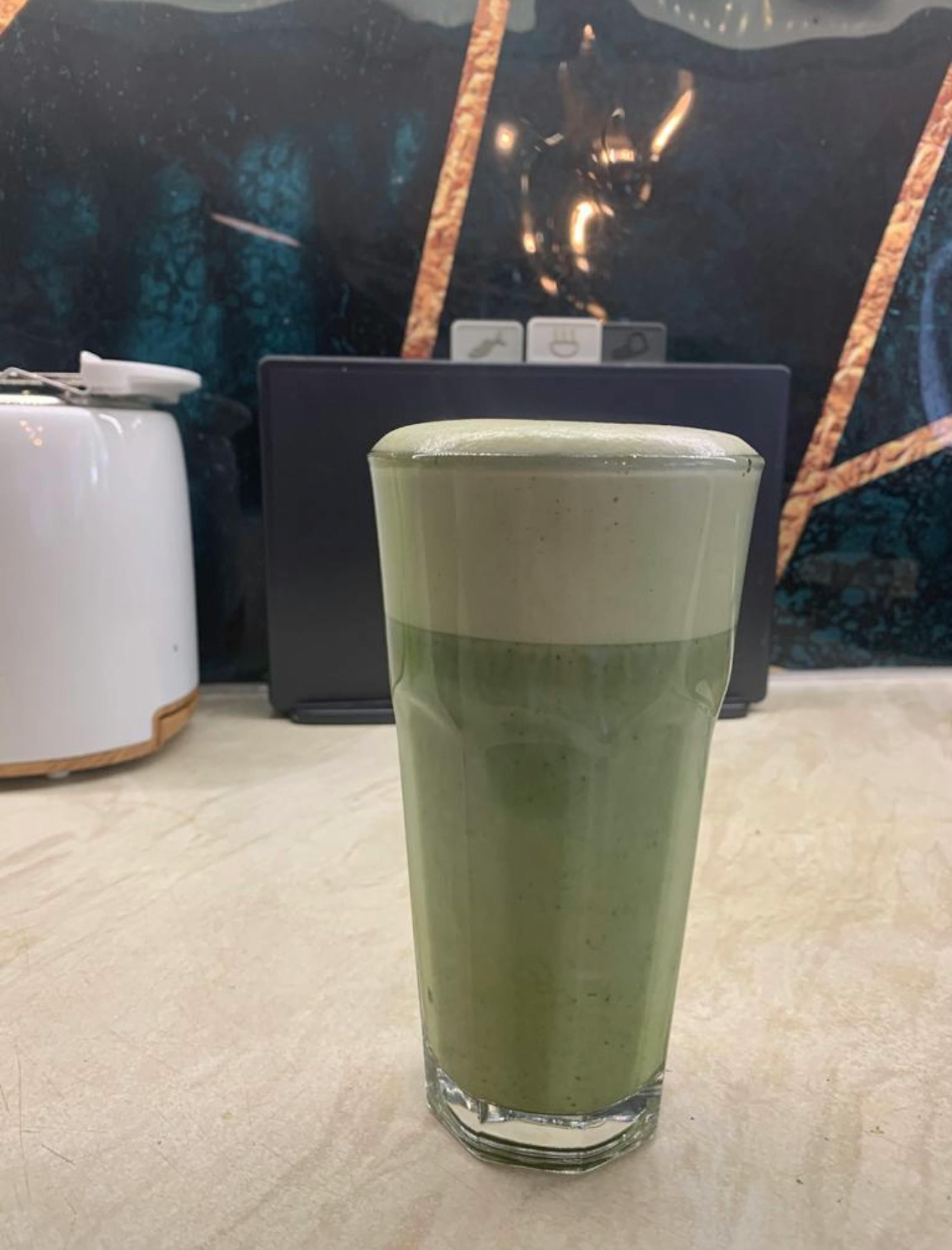 a tall glass filled with green liquid sits on a counter