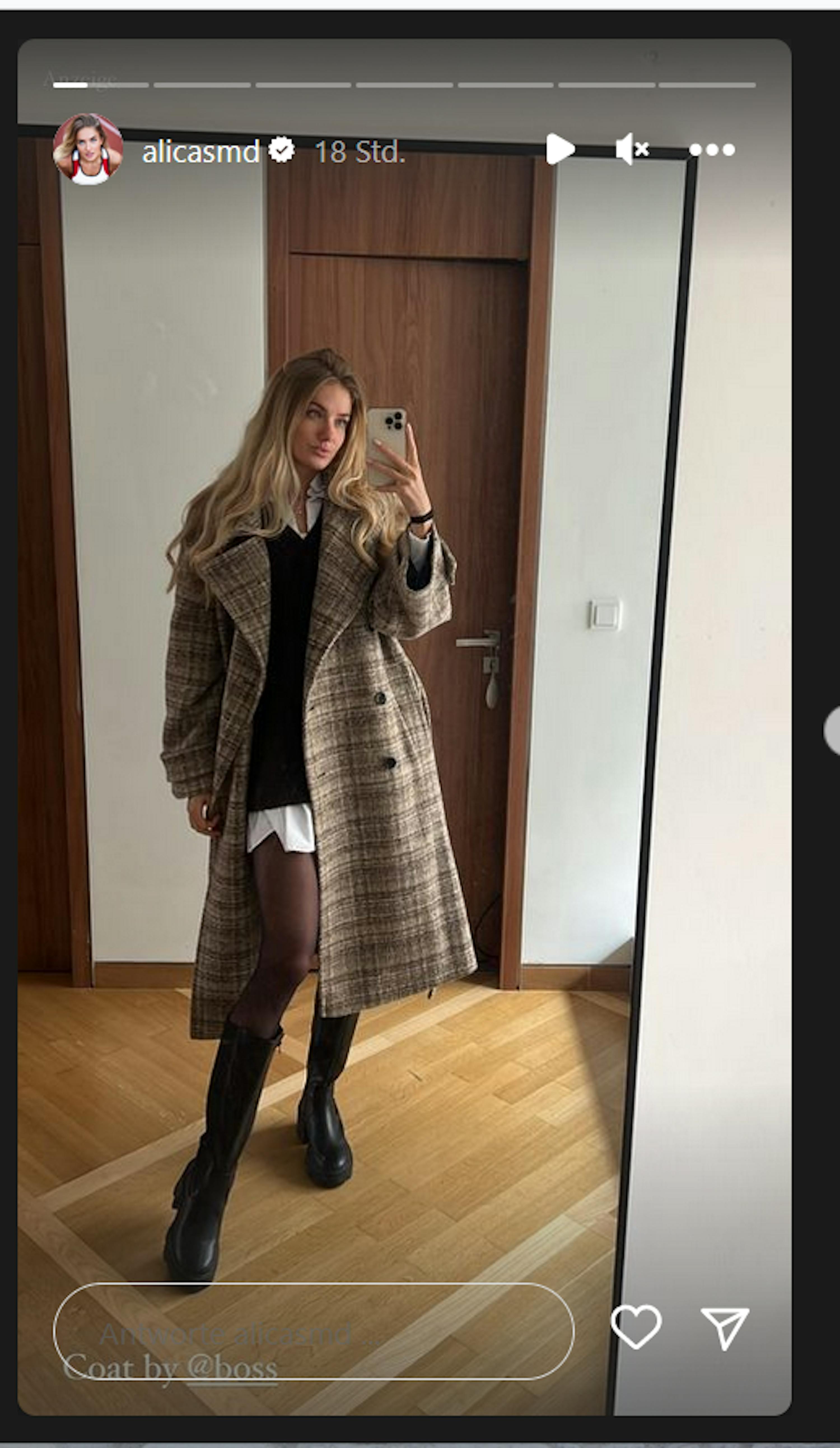 eine Frau in einem karierten Mantel und schwarzen Stiefeln nimmt ein selfie in einem Spiegel