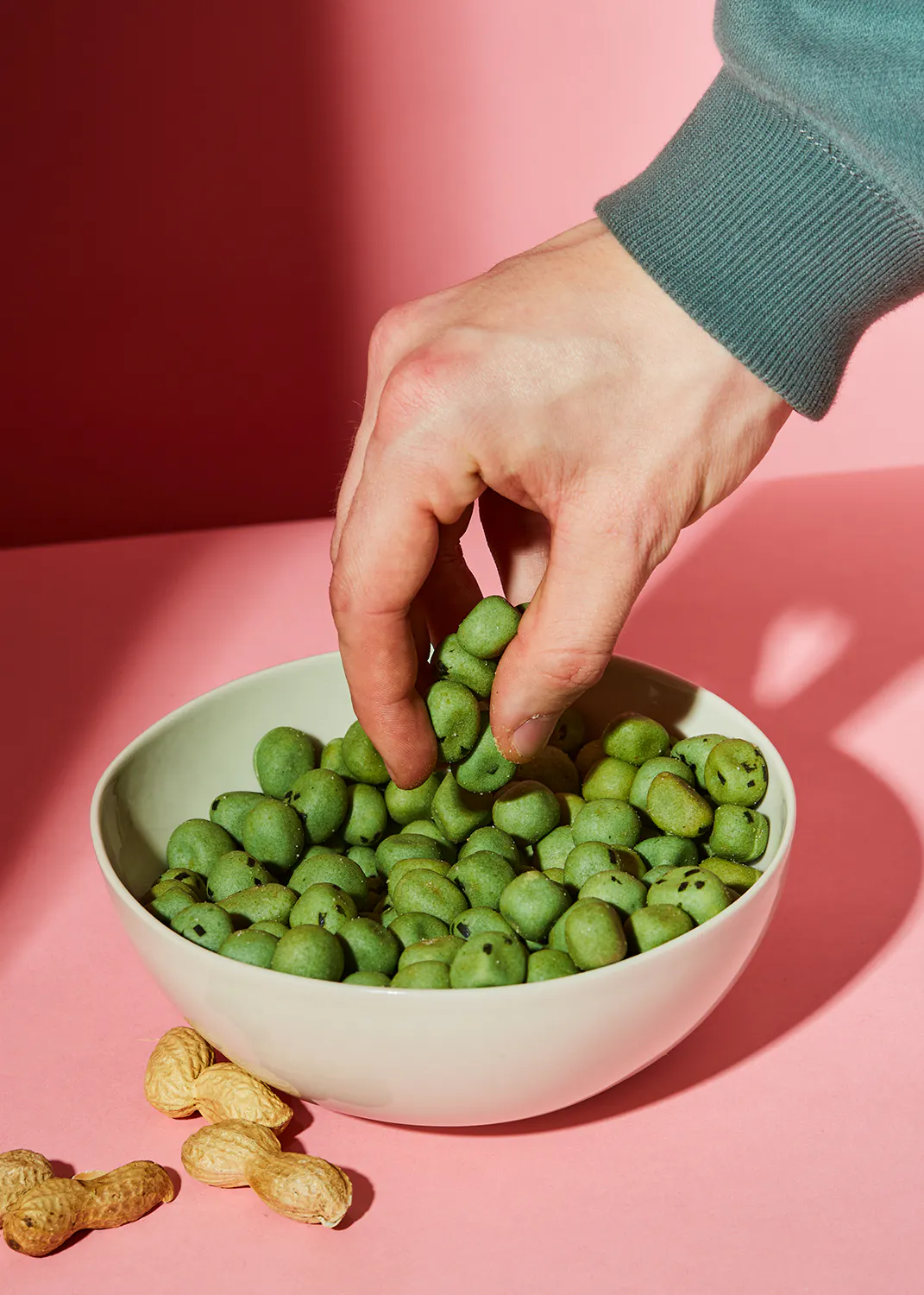 eine Person greift nach grünen Erdnüssen aus einer Schüssel