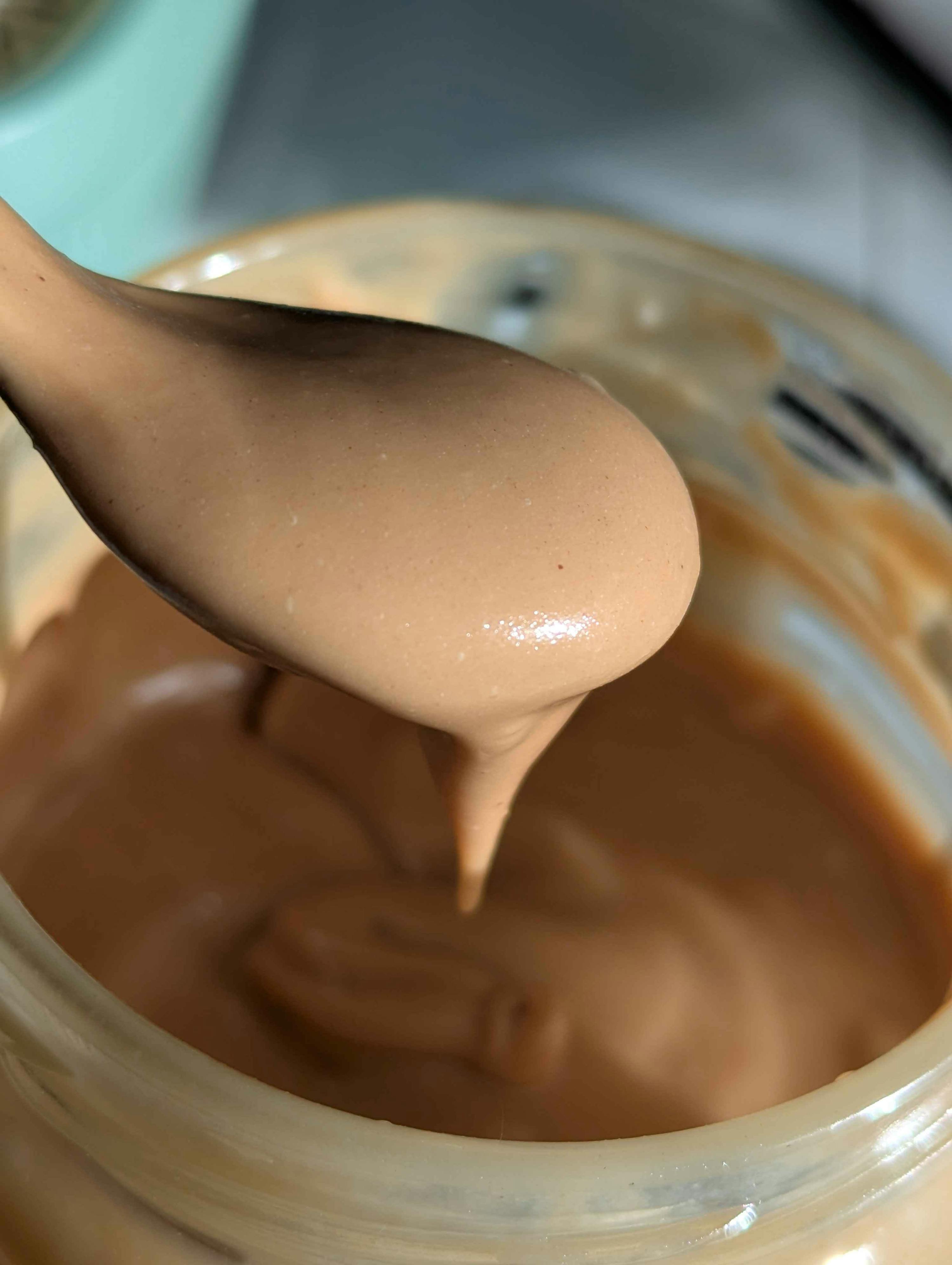 une cuillère remplie de beurre de cacahuète crémeux qui dégouline dans un pot.