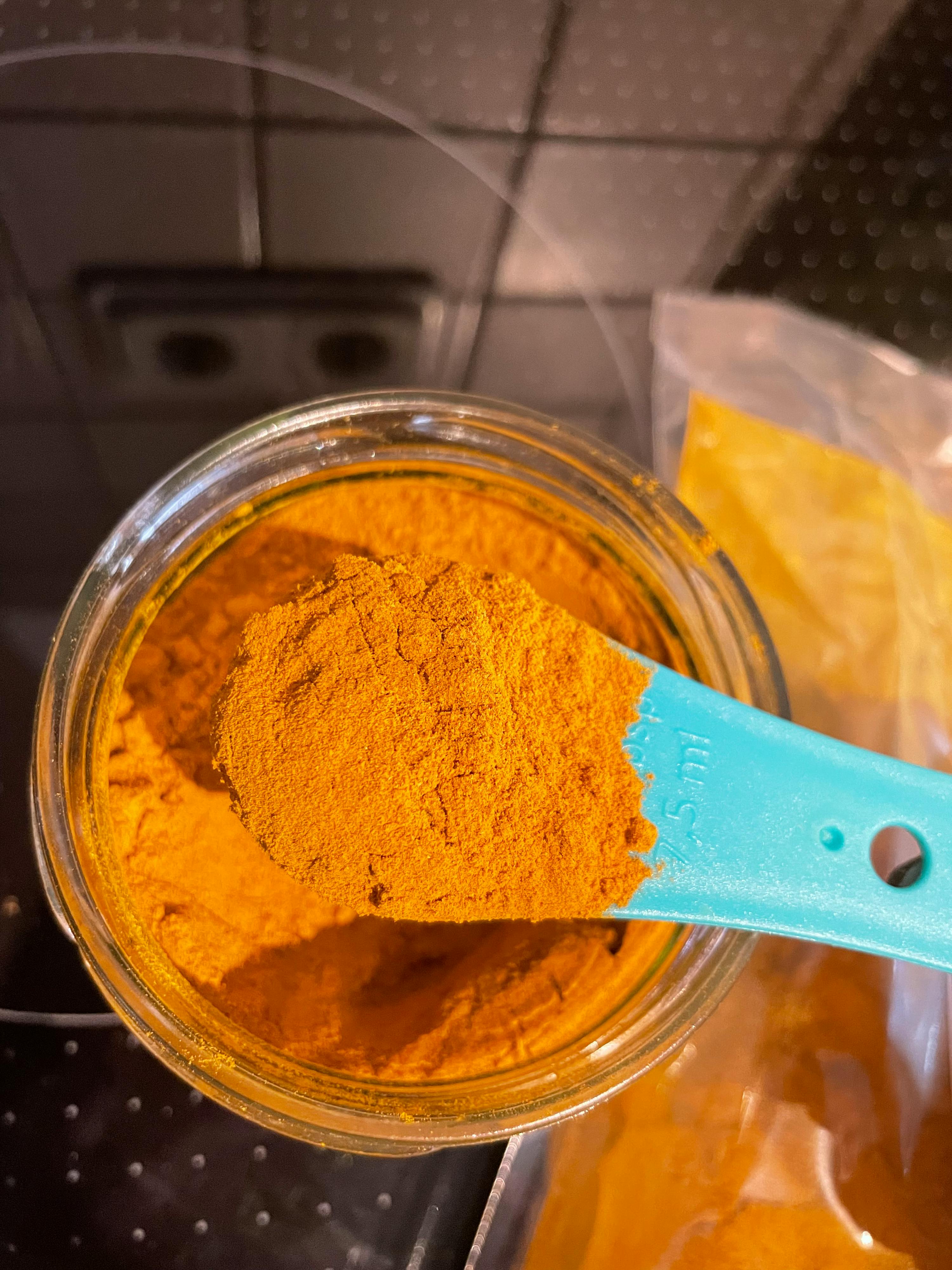 ein blauer Messlöffel hält einen Löffel aus einem Glas mit Gewürzen