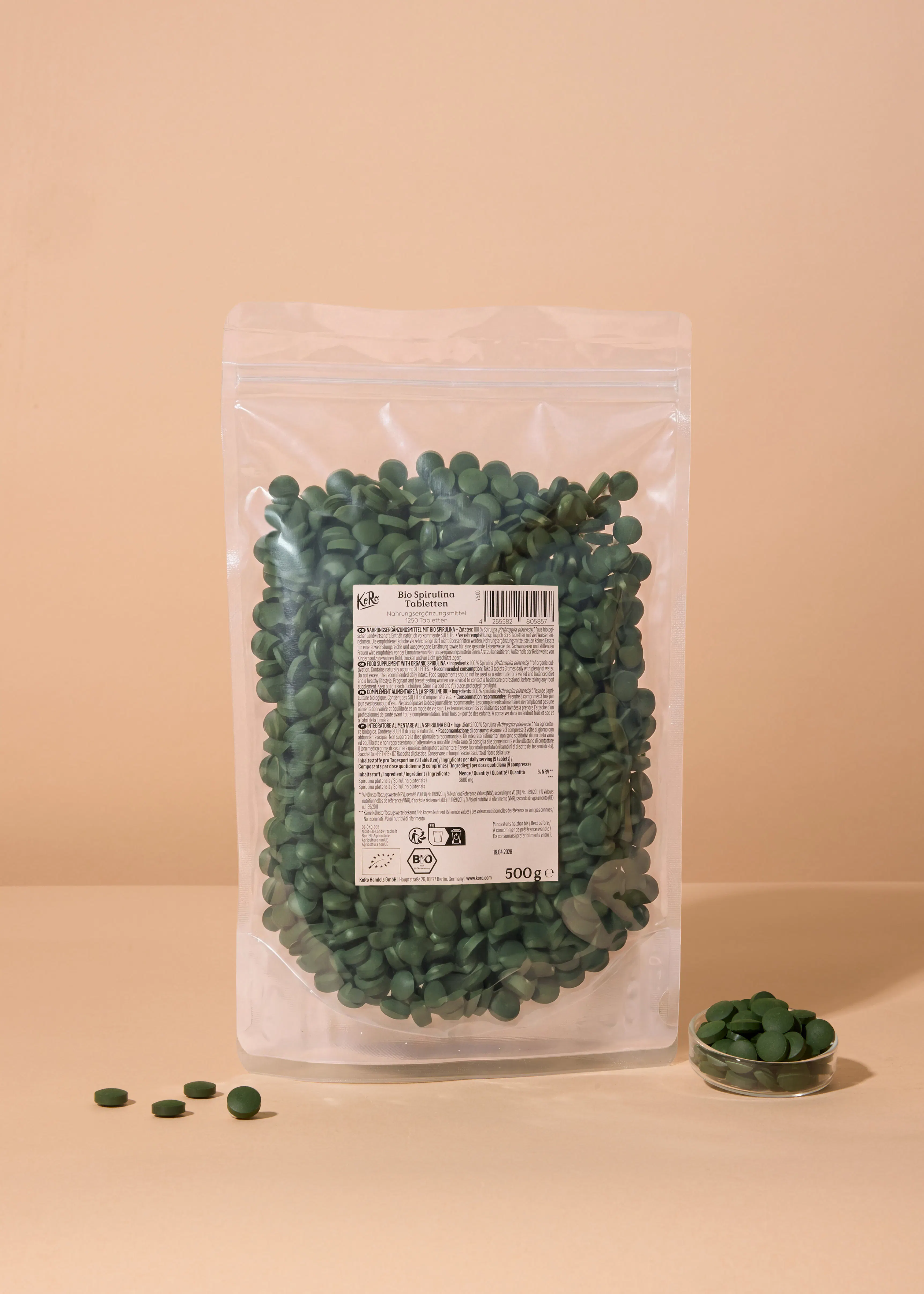 un sac transparent de 500g de comprimés de spiruline bio verts, avec quelques comprimés renversés et un petit bol de comprimés à côté.