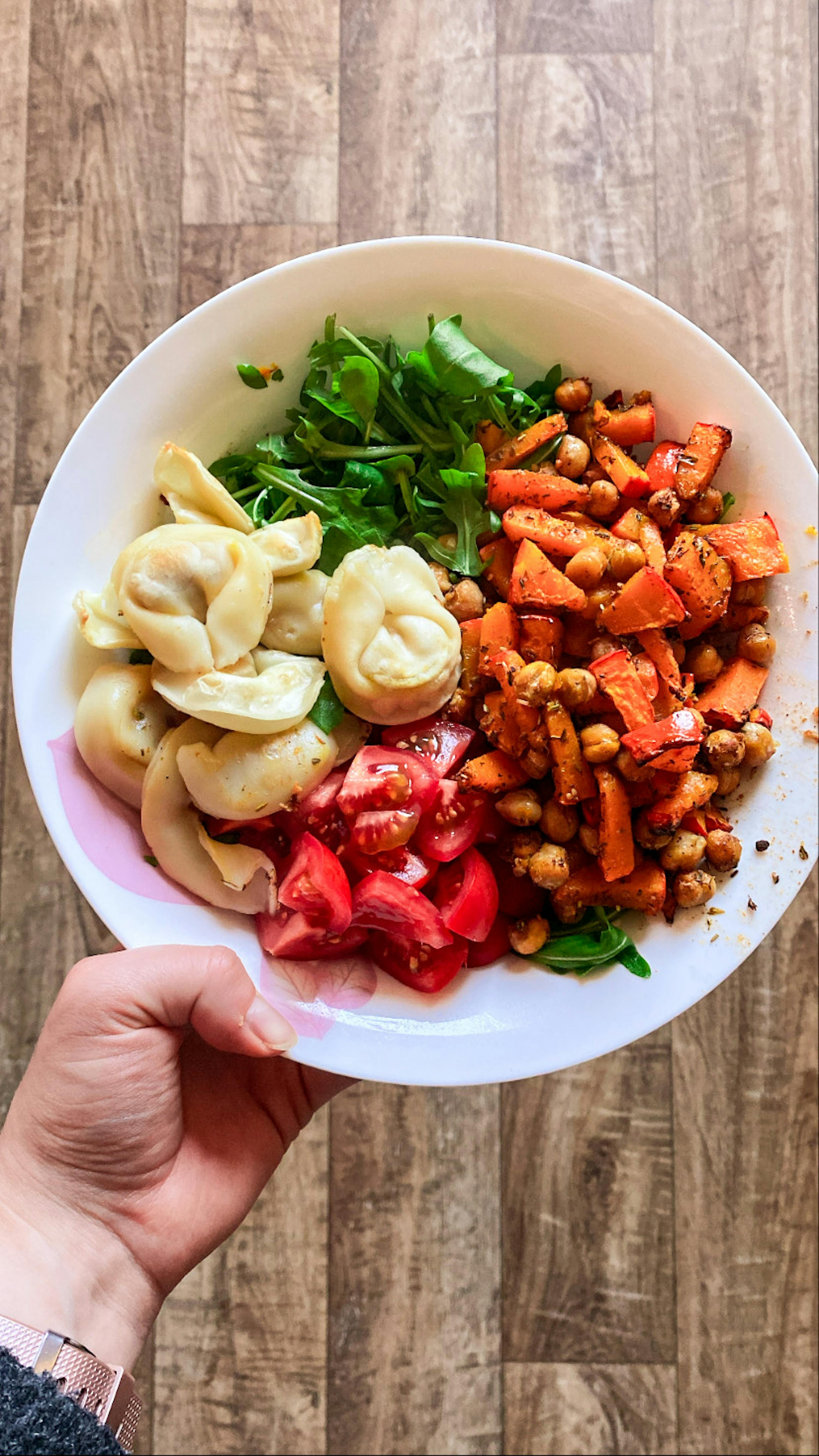 a person is holding a plate of food including ravioli tomatoes and chickpeas