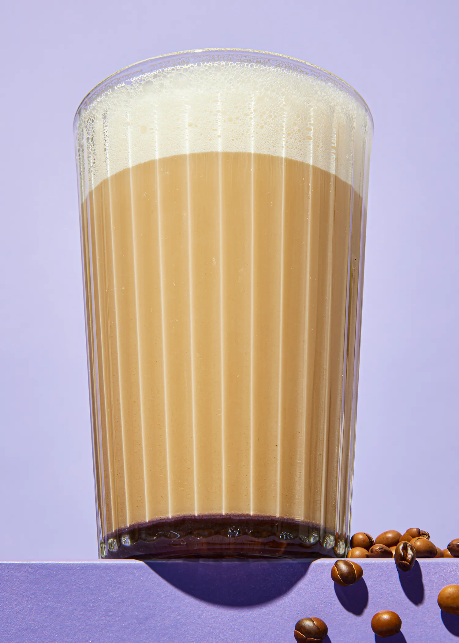 un vaso de café está sobre un fondo púrpura junto a granos de café