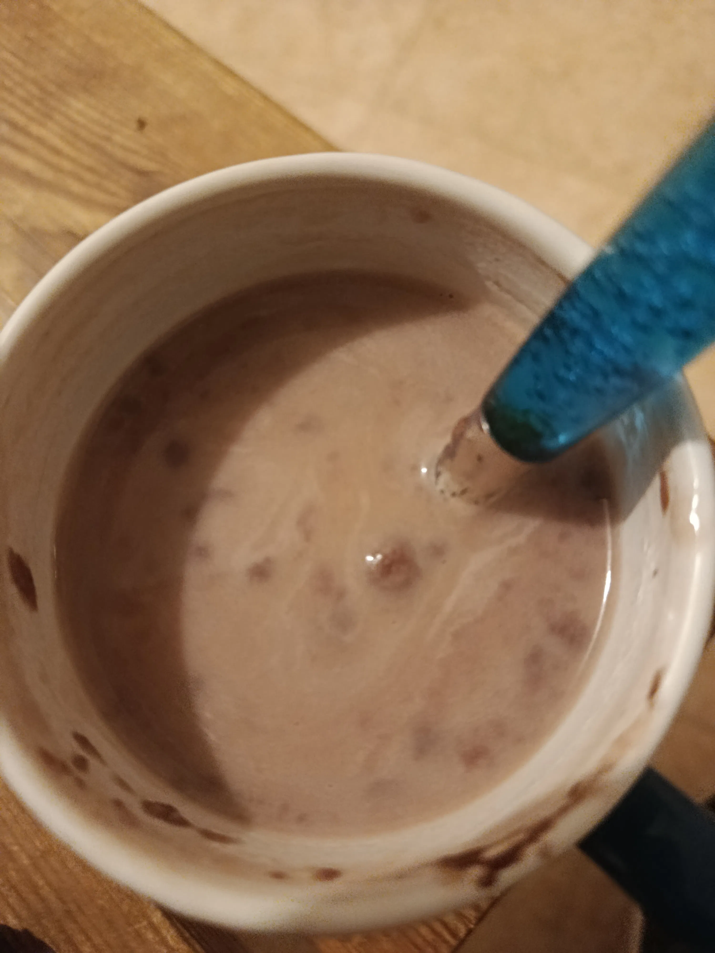 a mug of hot chocolate with a blue spoon on a wooden surface.