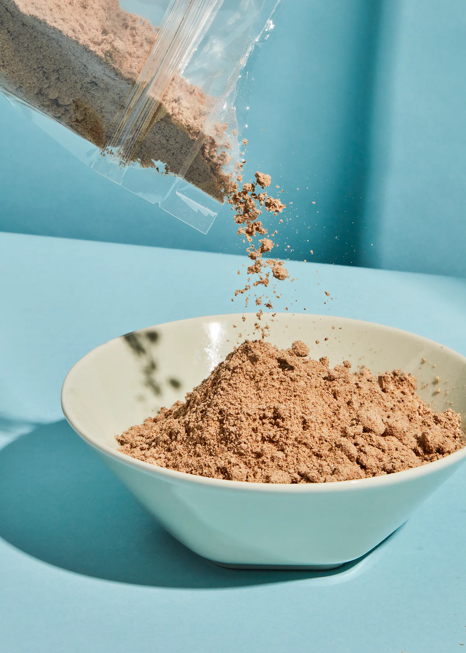 eine weiße Schüssel mit braunem Pulver wird aus einer Plastiktüte gegossen