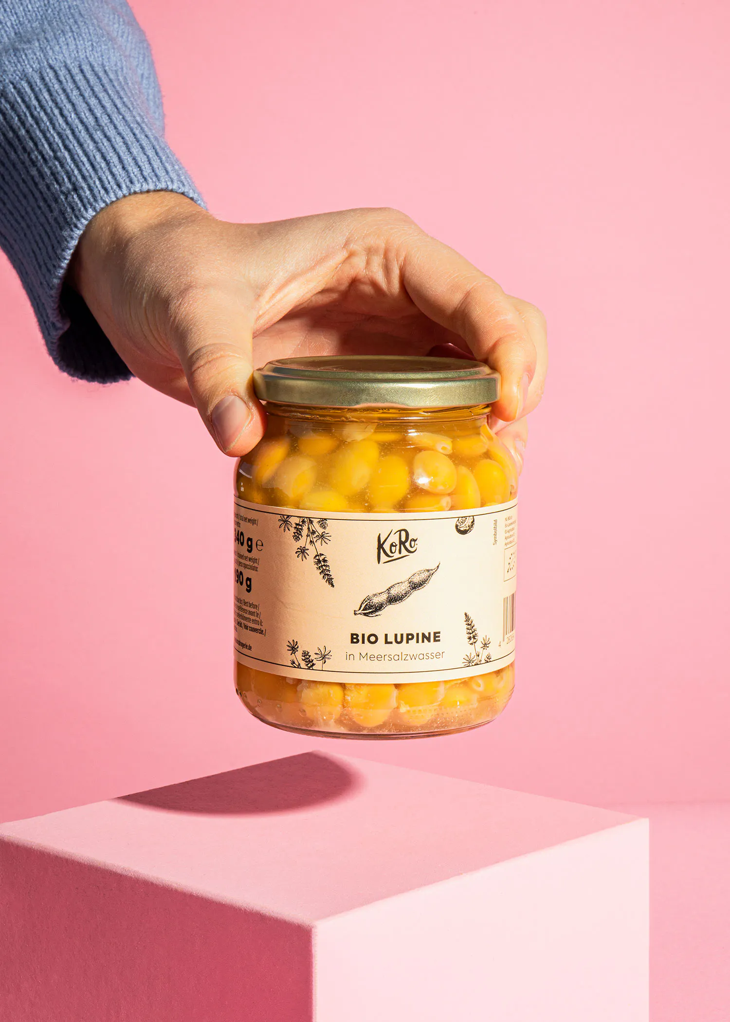 une personne tient un bocal de lupin bio sur un fond rose