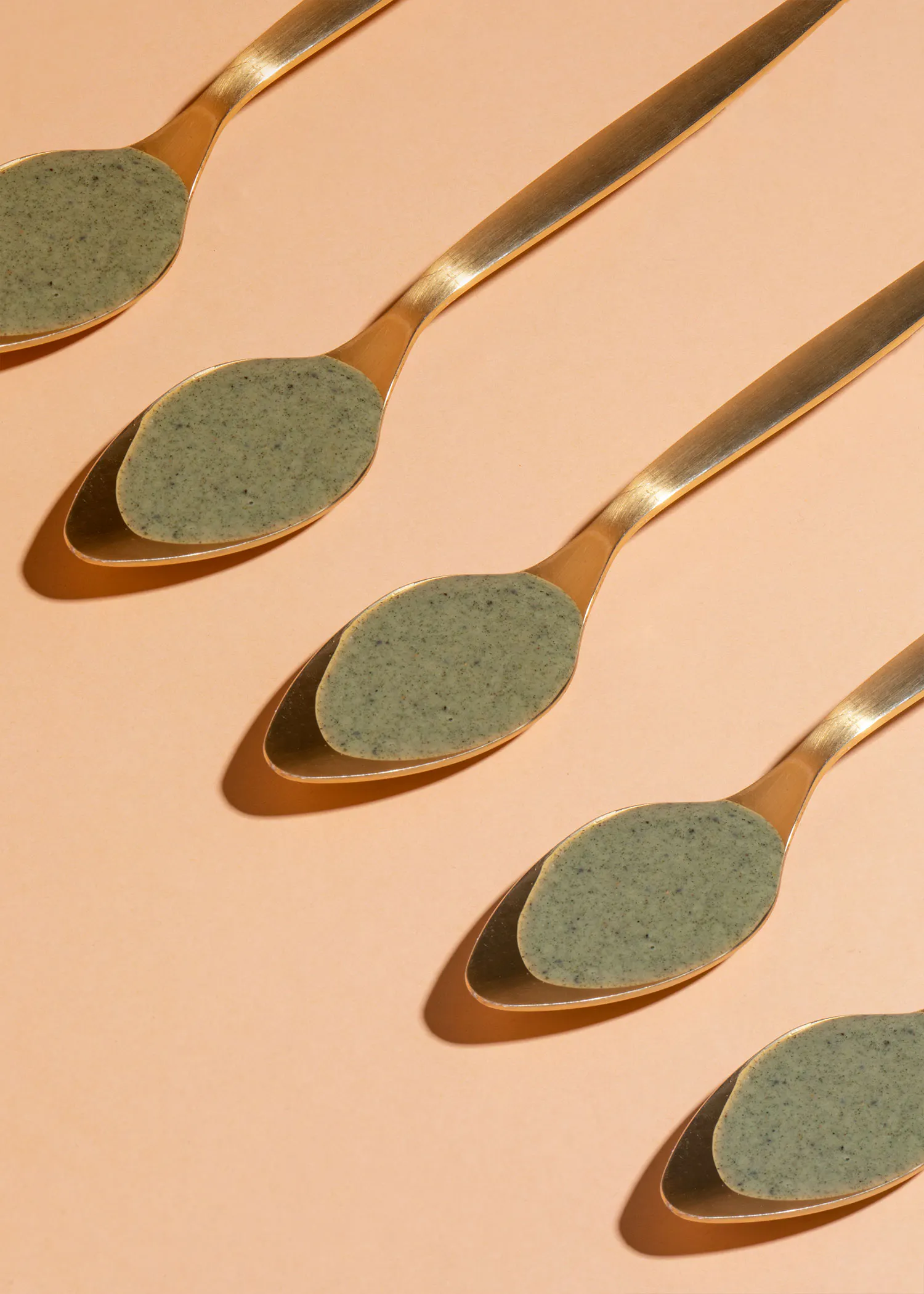 a row of gold spoons with green powder on them