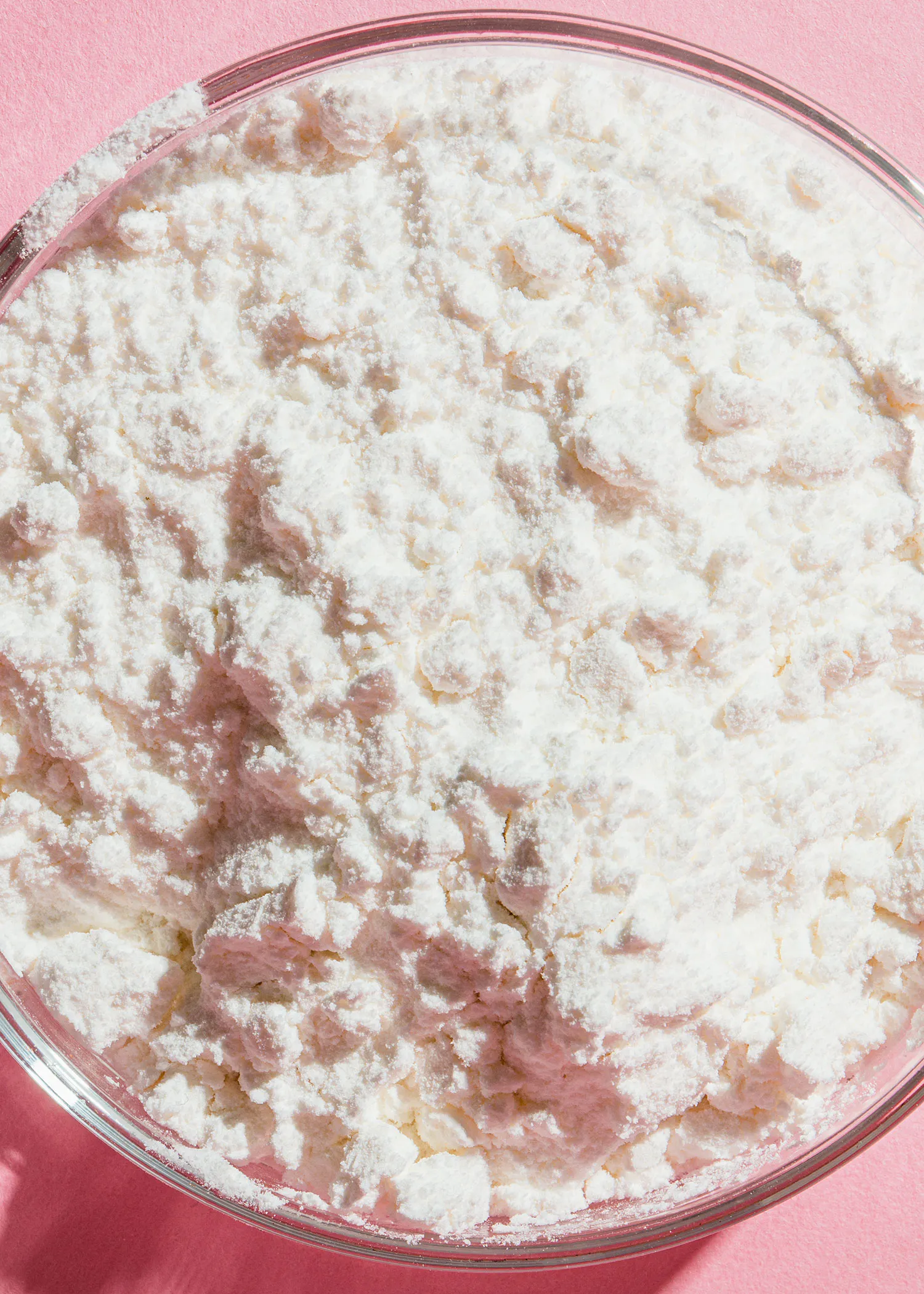 un bol en verre rempli de farine blanche sur fond rose