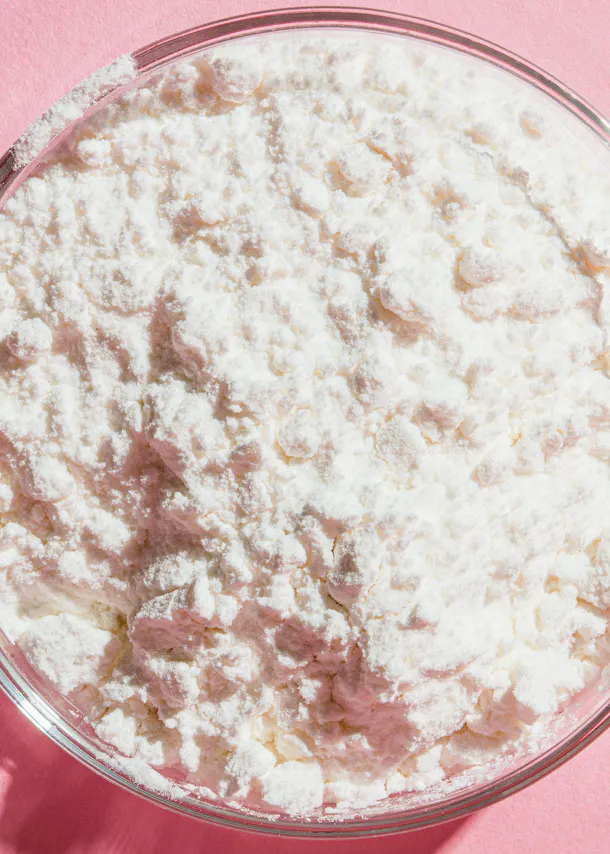 eine Glasschüssel mit weißem Pulver auf einem rosa Hintergrund