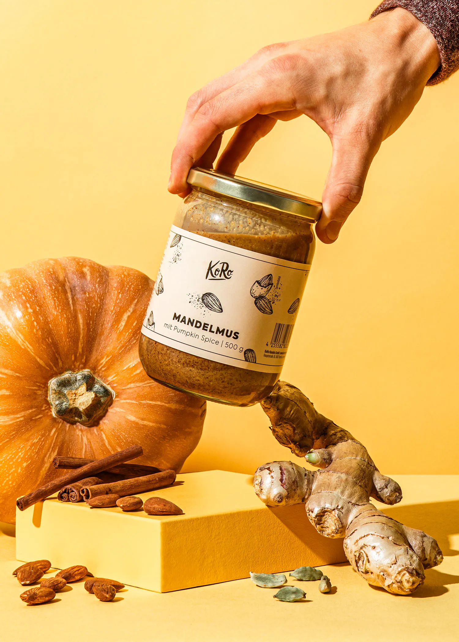 une personne tient un bocal de mandelmus à côté d' une citrouille et d' un gingembre