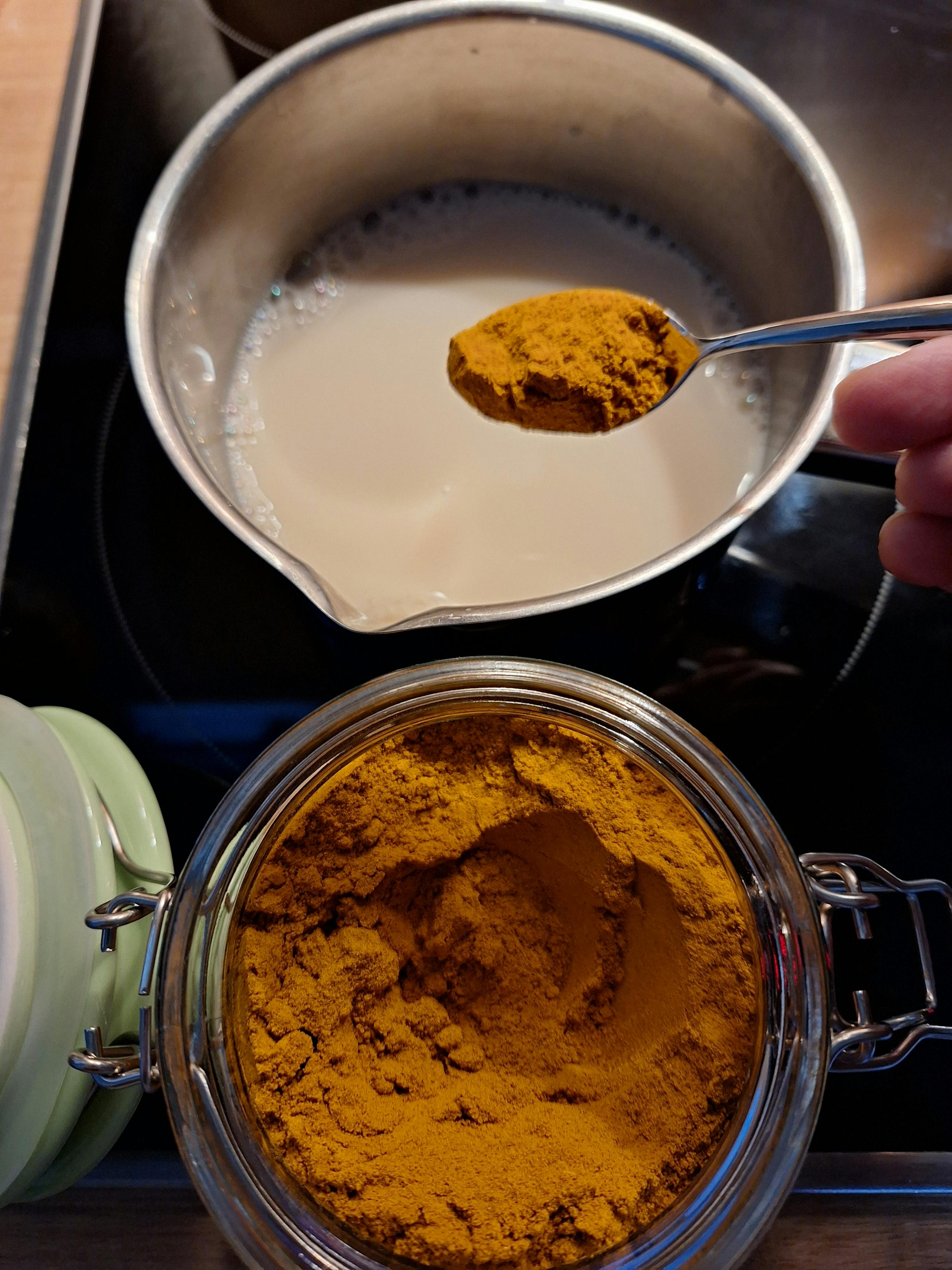 eine Person gießt ein Löffelcurrypulver in einen Topf