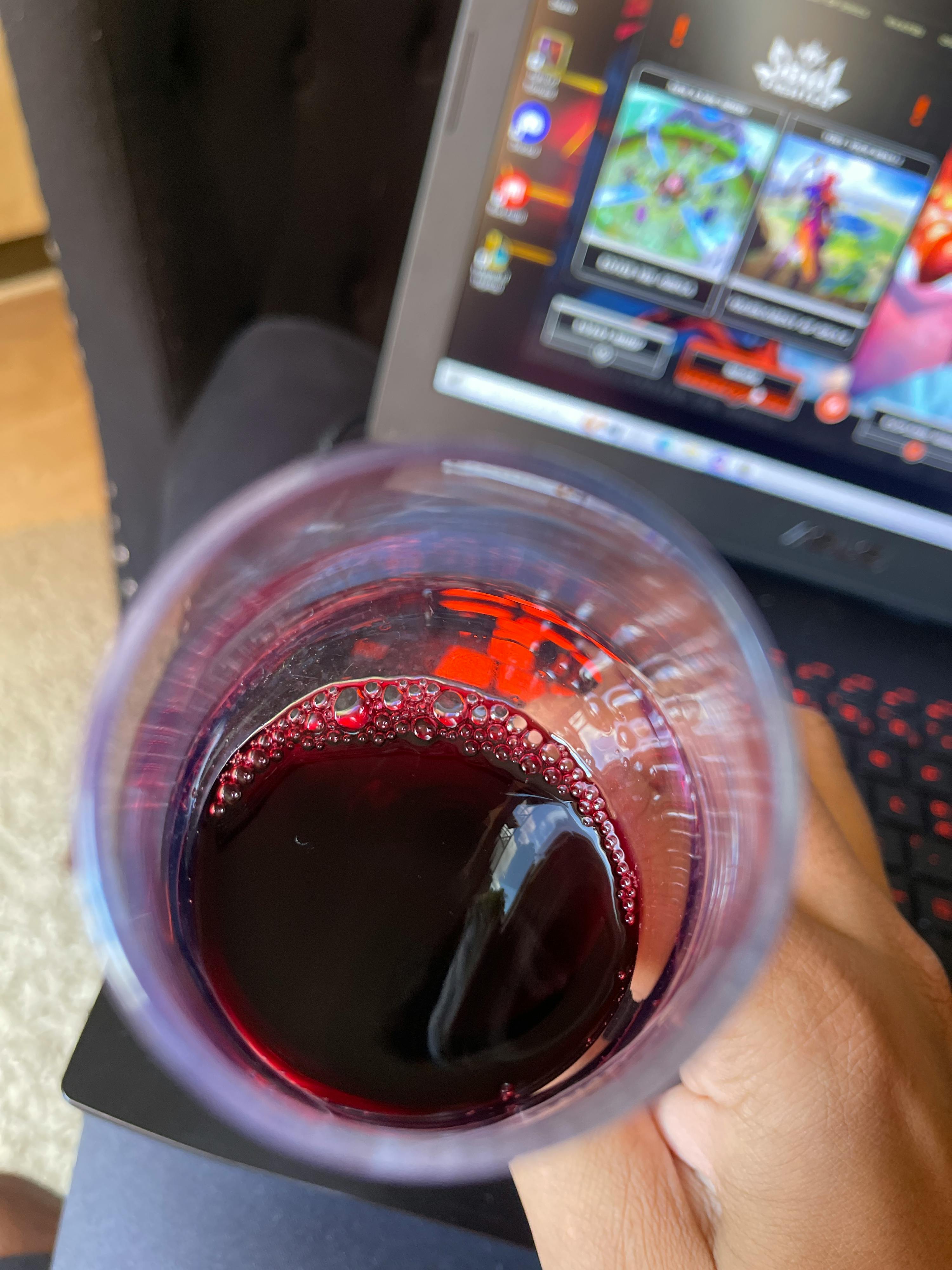 une personne tient un verre de vin devant un ordinateur portable