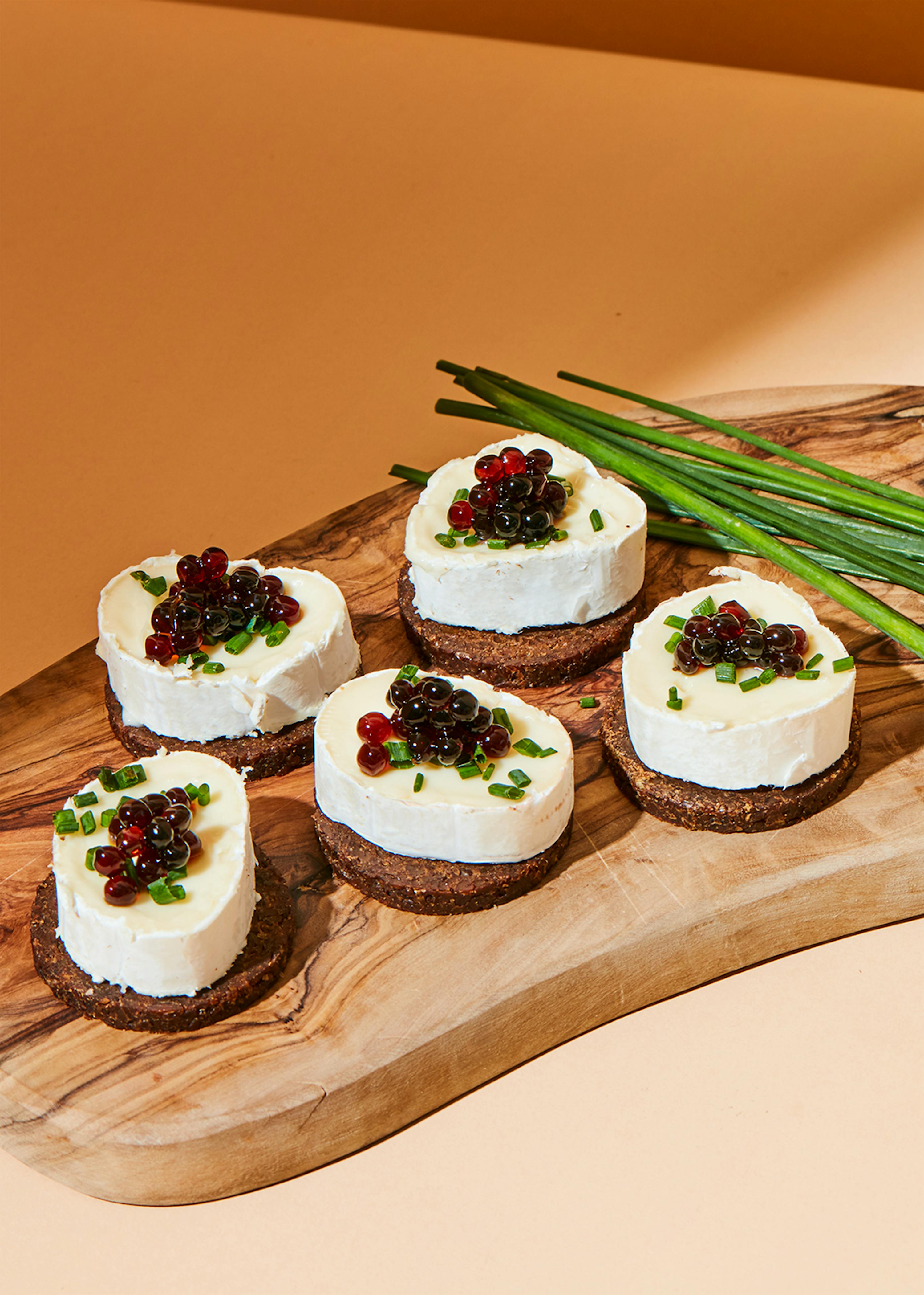 a wooden cutting board with slices of cheese and berries on top