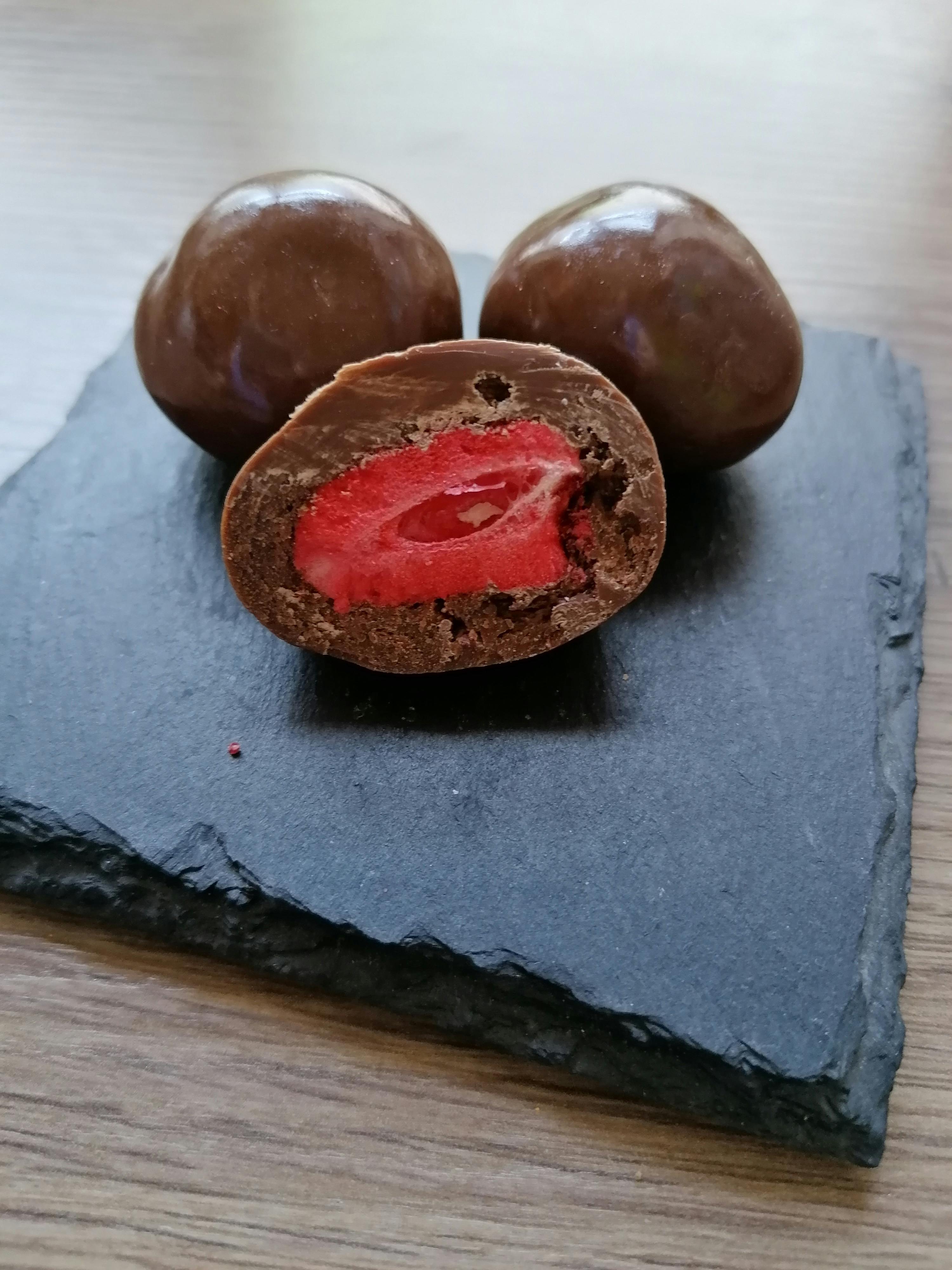 a chocolate covered strawberry is cut in half on a slate plate