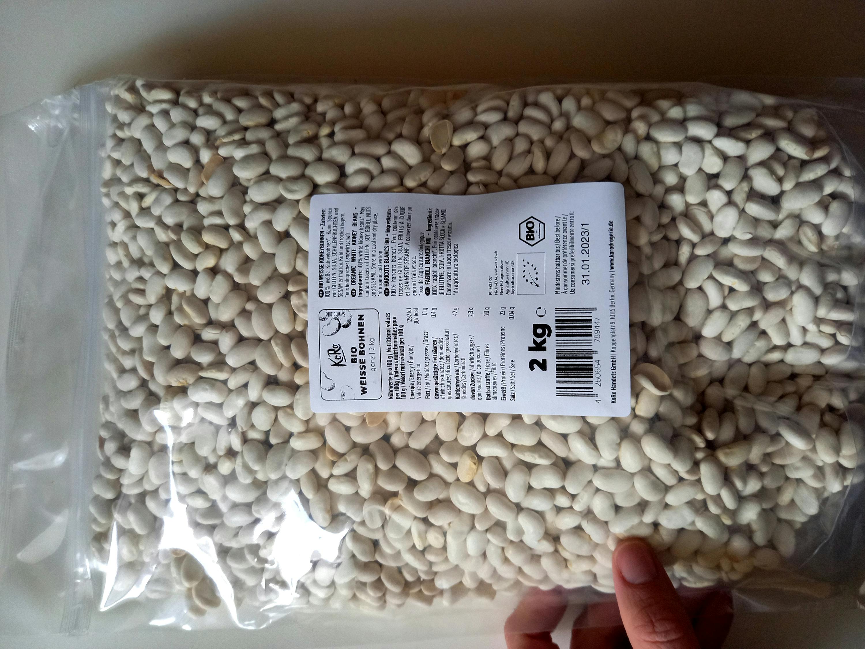 eine Person hält einen Plastikbeutel mit weißen Bohnen in der Hand