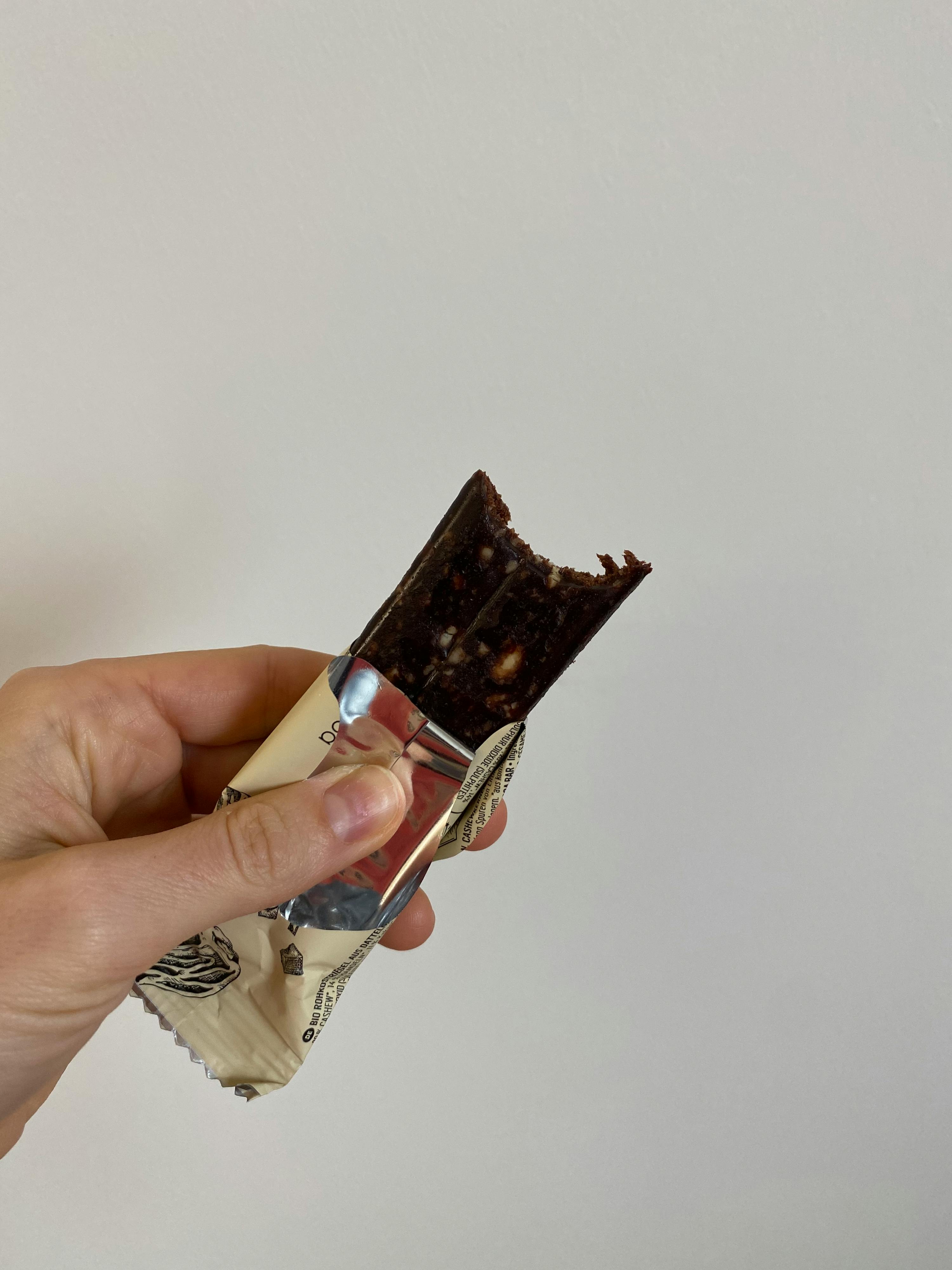 a hand is holding a chocolate bar with a bite taken out of it