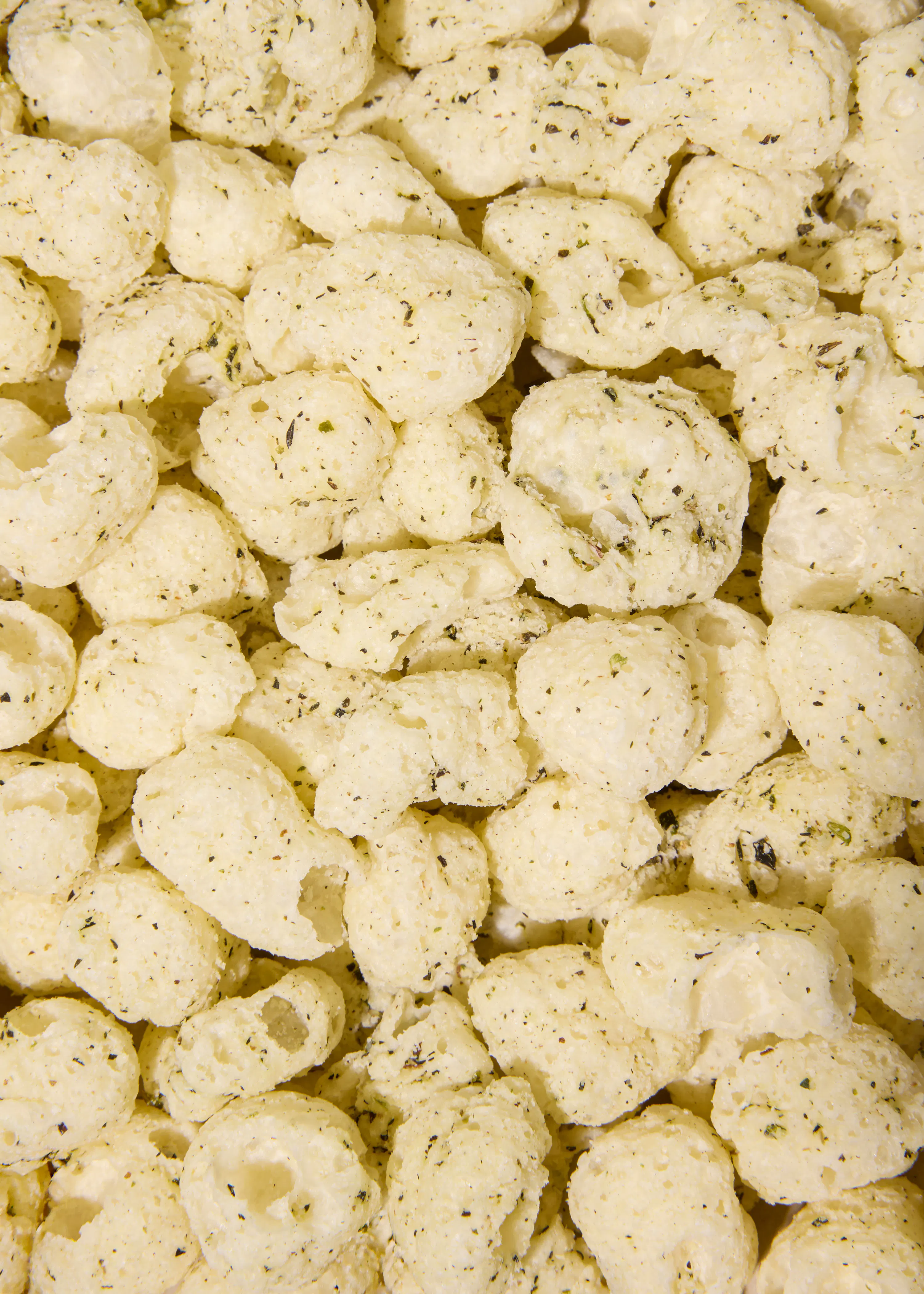 primo piano di snack di mais soffiato di colore chiaro cosparsi di erbe aromatiche.