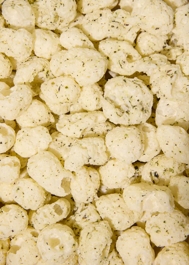 primo piano di snack di mais soffiato di colore chiaro cosparsi di erbe aromatiche.
