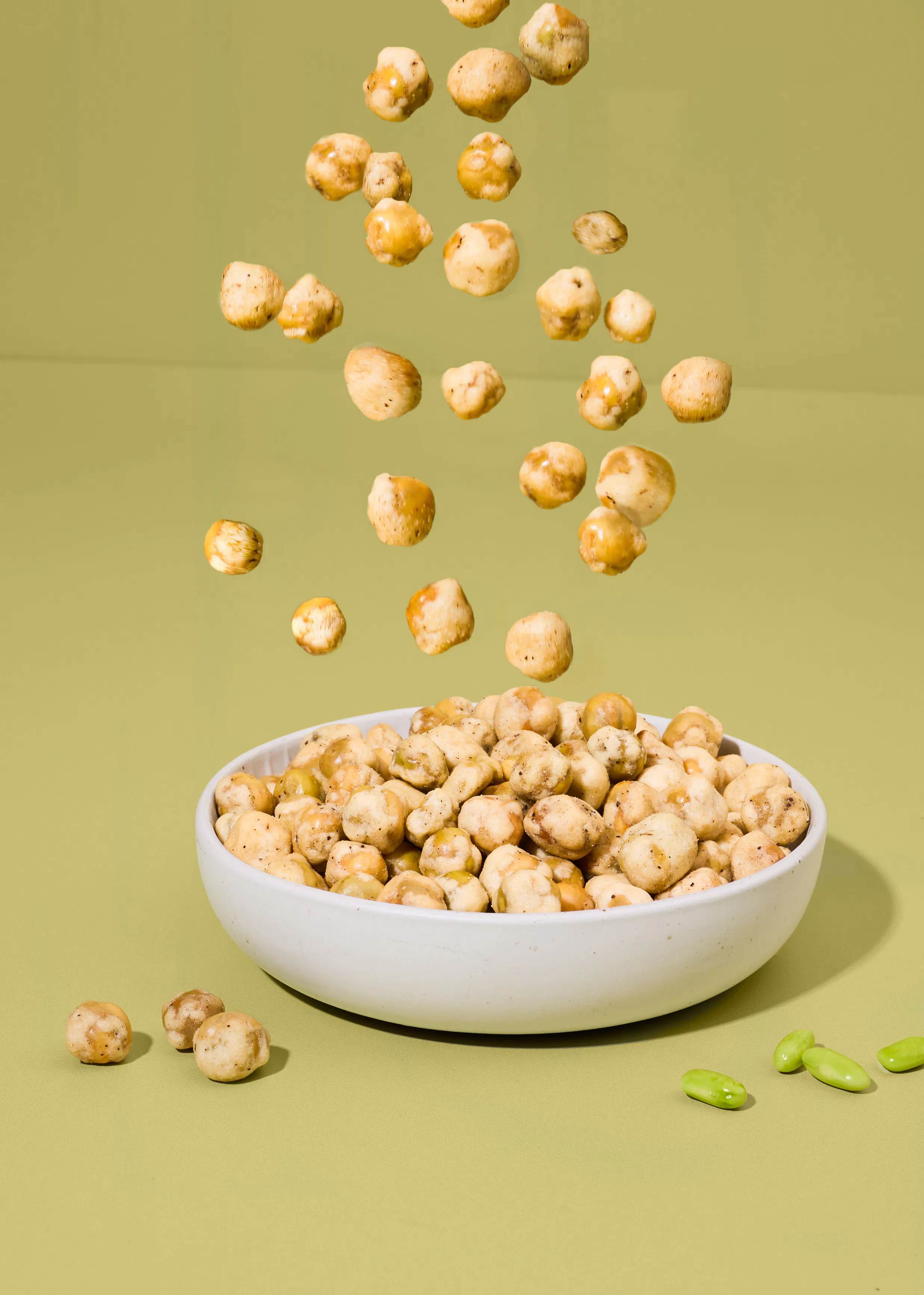 des pois chiches grillés tombent dans un bol blanc posé sur un fond vert clair.