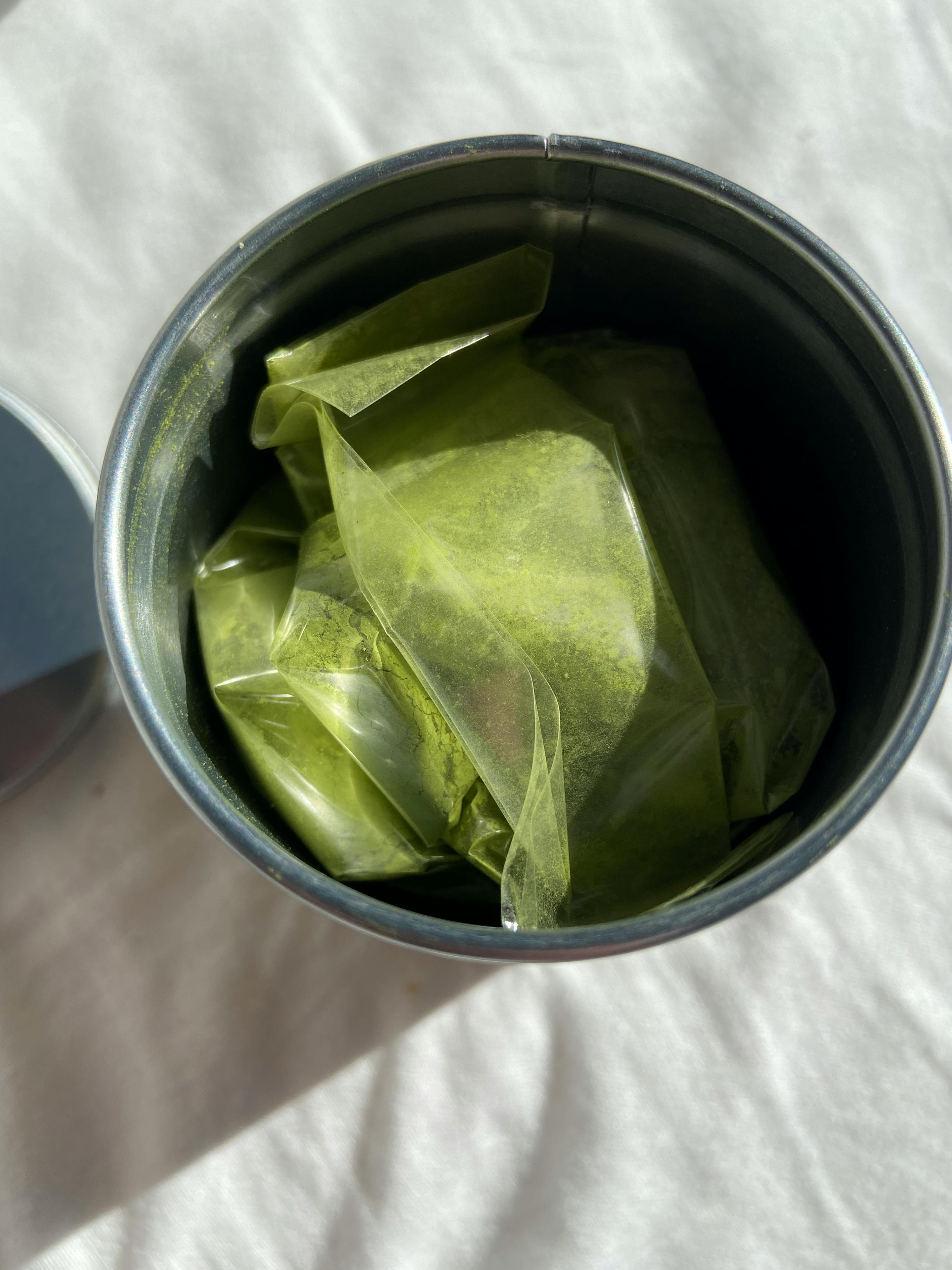 a tin filled with green powder is sitting on a white cloth