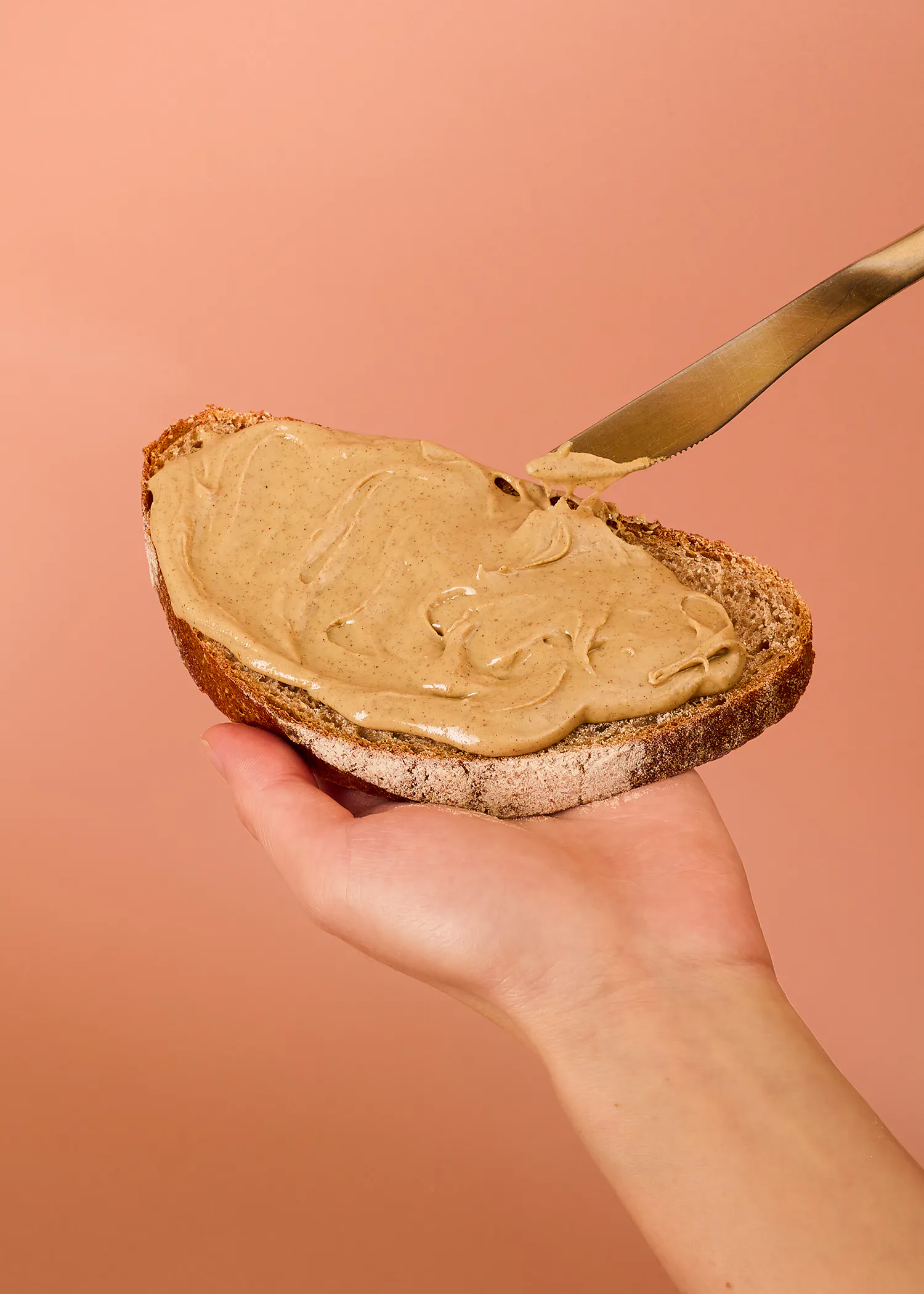 eine hand hält eine scheibe vollkornbrot, die mit einer cremigen nussbutter bestrichen wird.