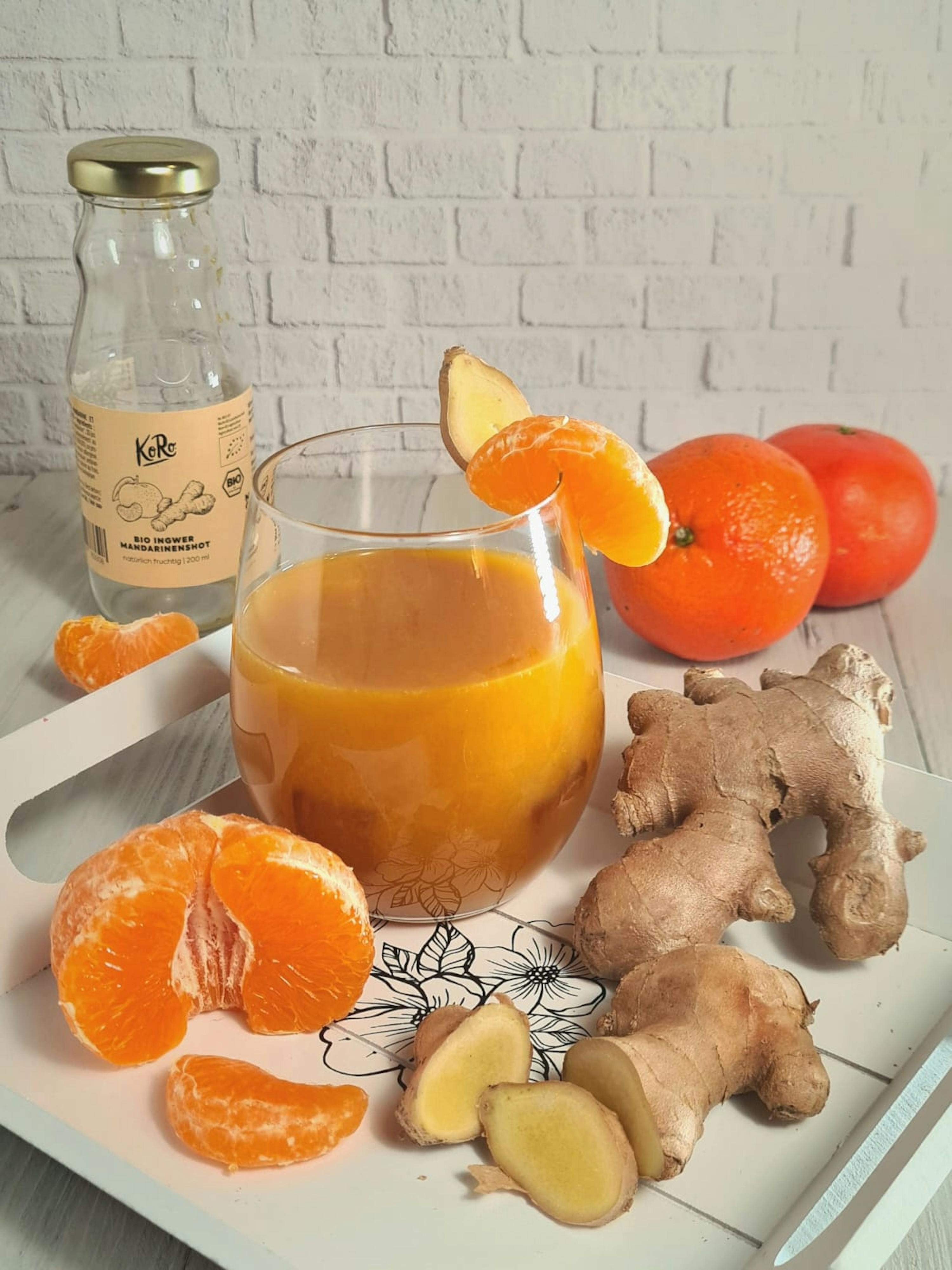 un verre de jus de gingembre est assis sur un plateau avec des oranges et du gingembre