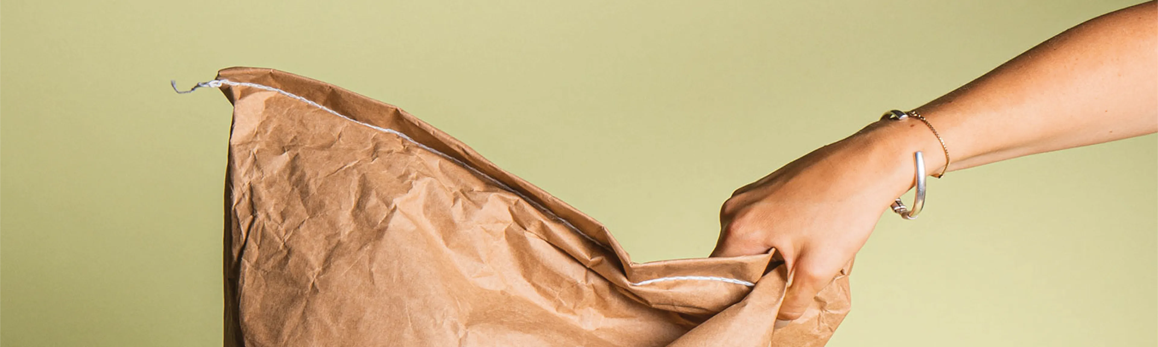 une main tenant un sac en papier brun avec un bracelet argenté
