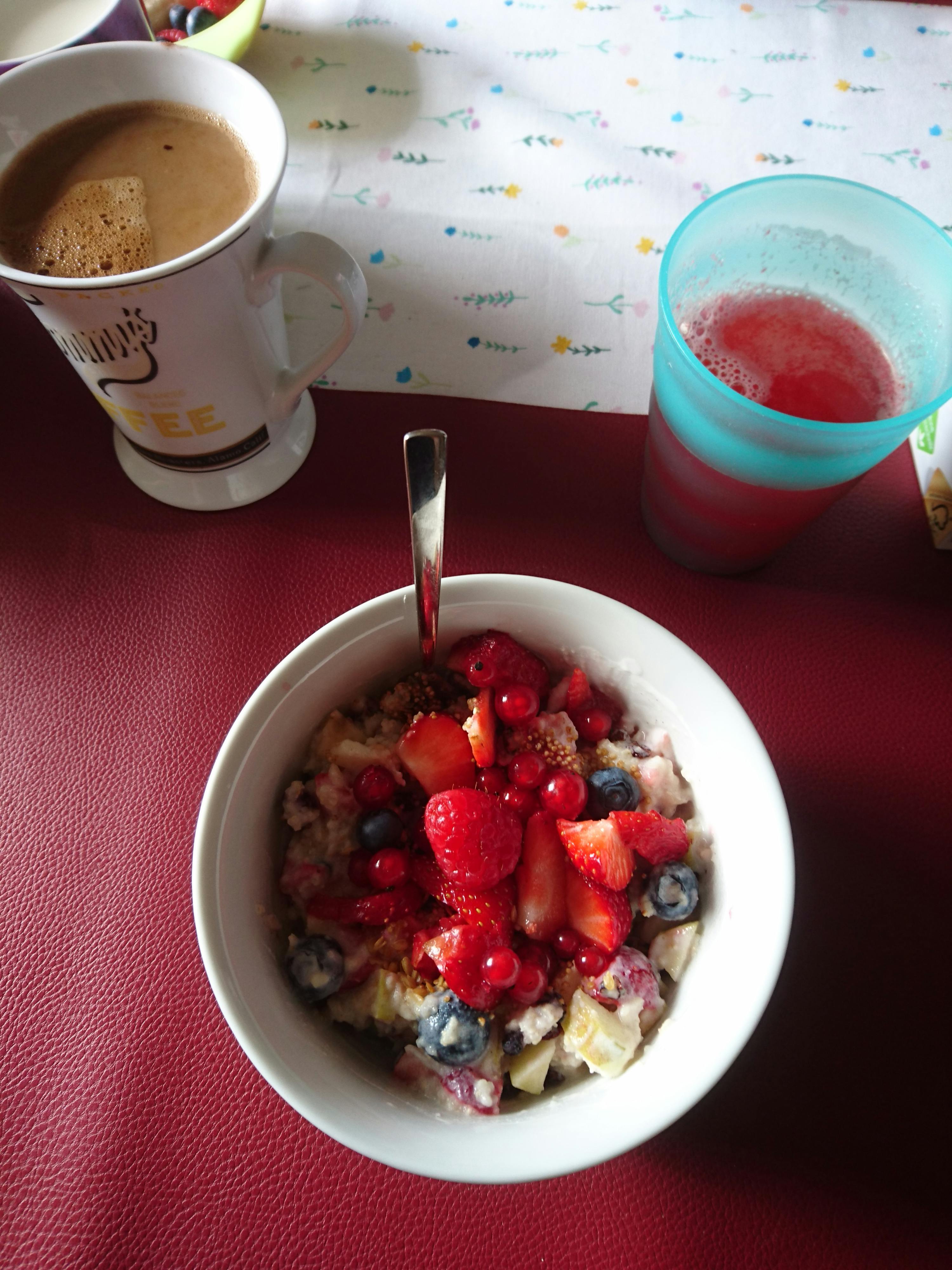 a bowl of oatmeal with strawberries and blueberries next to a cup of coffee