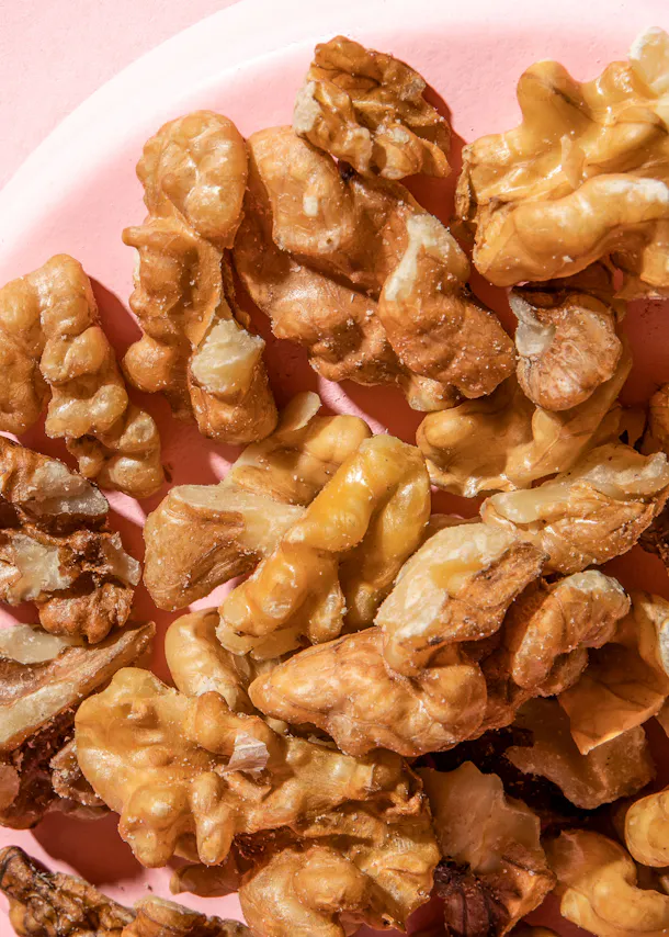 une assiette remplie de noix sur fond rose