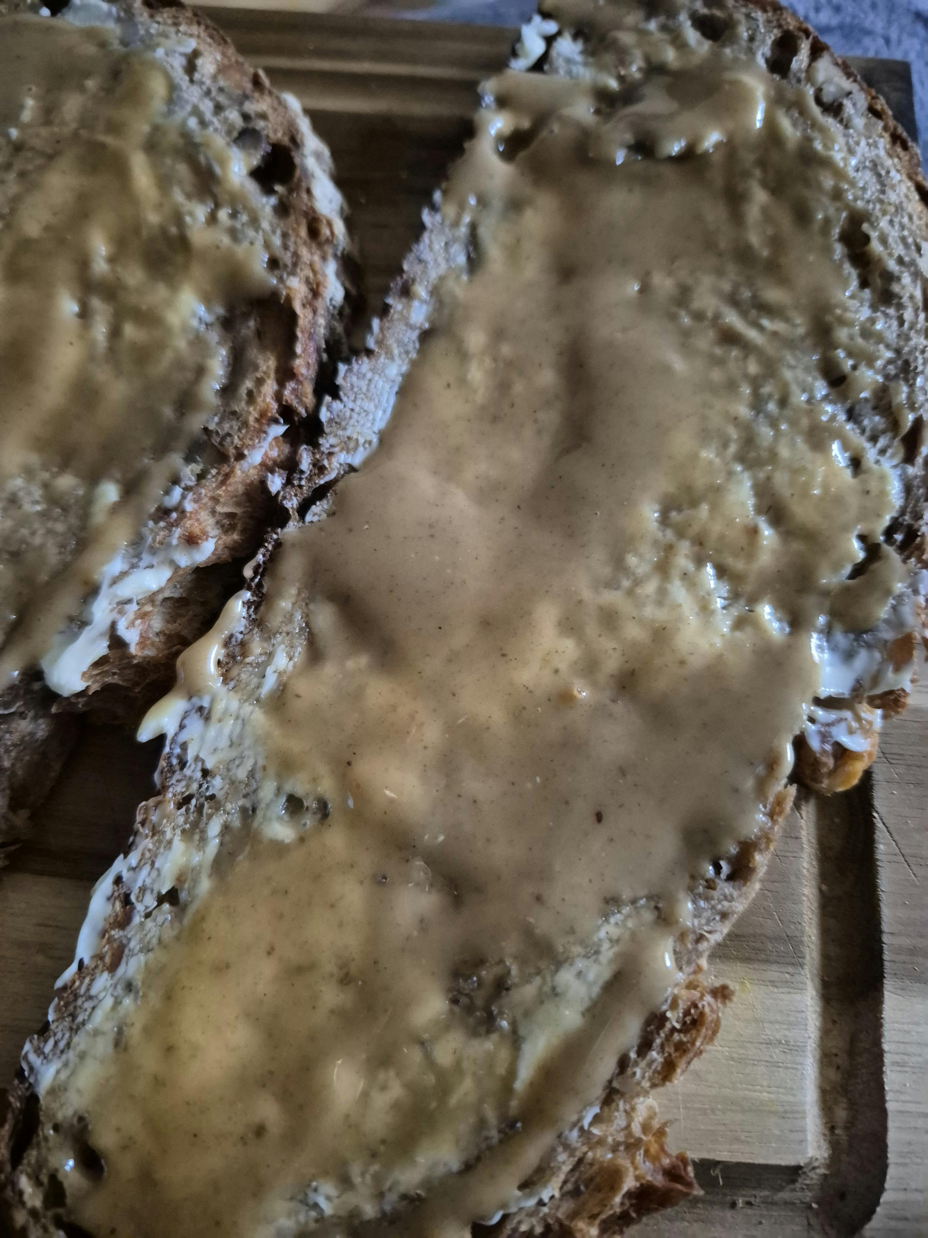 due fette di pane scuro con una spalmata densa e cremosa di crema spalmabile su un tagliere di legno.