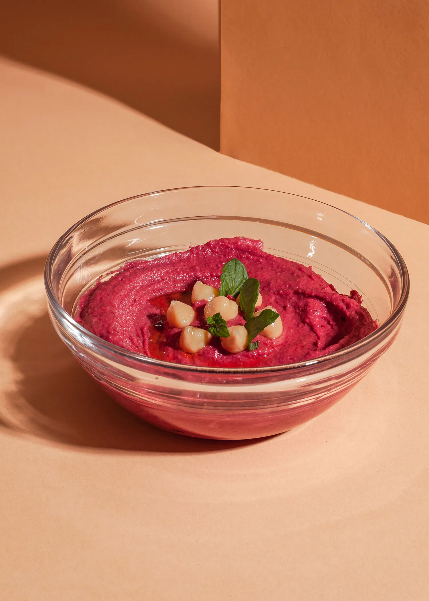 un bol en verre rempli de hummus avec des haricots et des feuilles de menthe