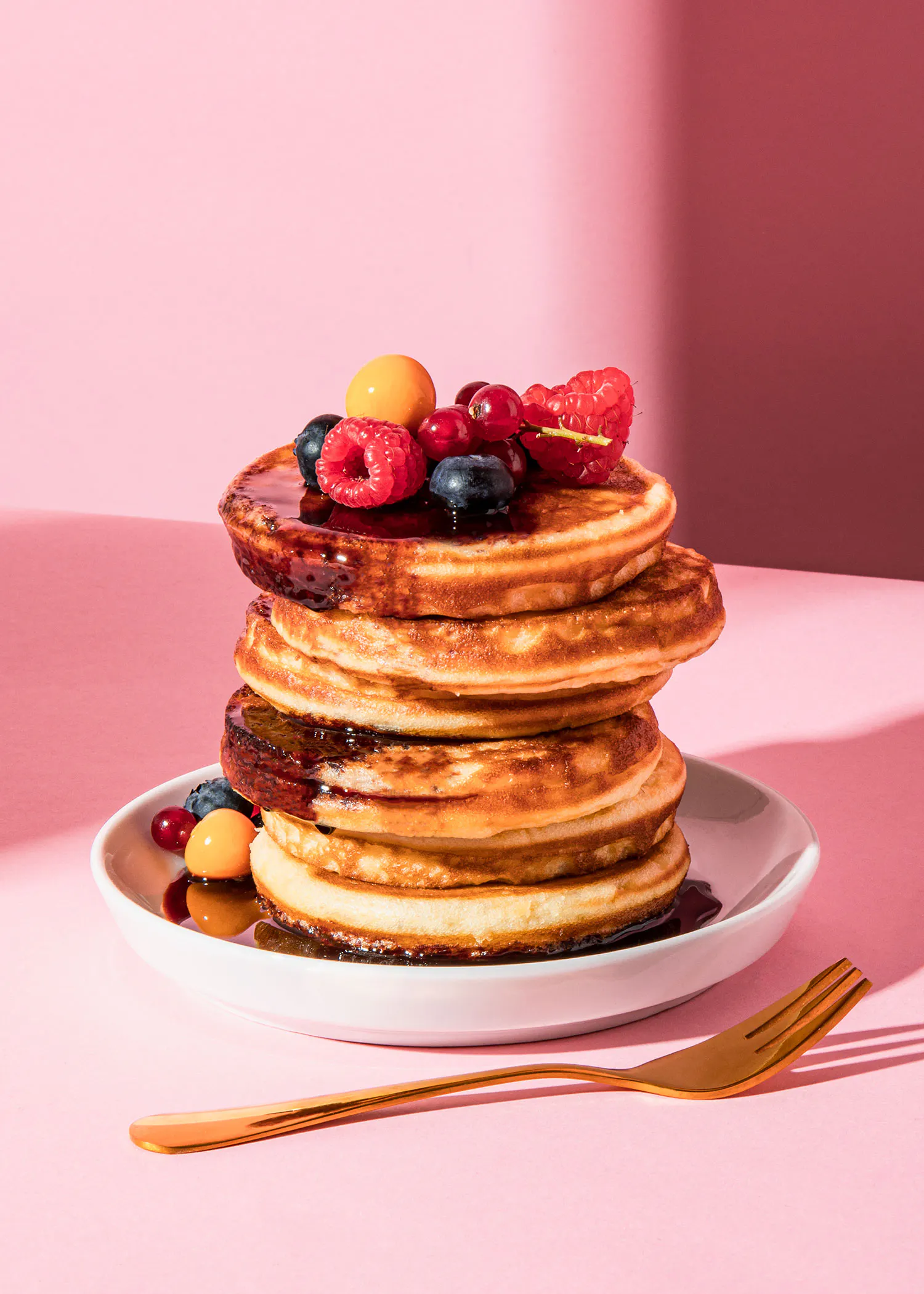 une pile de crêpes avec des baies et du sirop sur une assiette avec une fourchette
