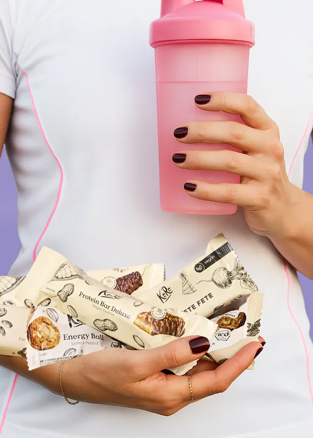 a woman is holding a pink shaker and a protein bar deluxe