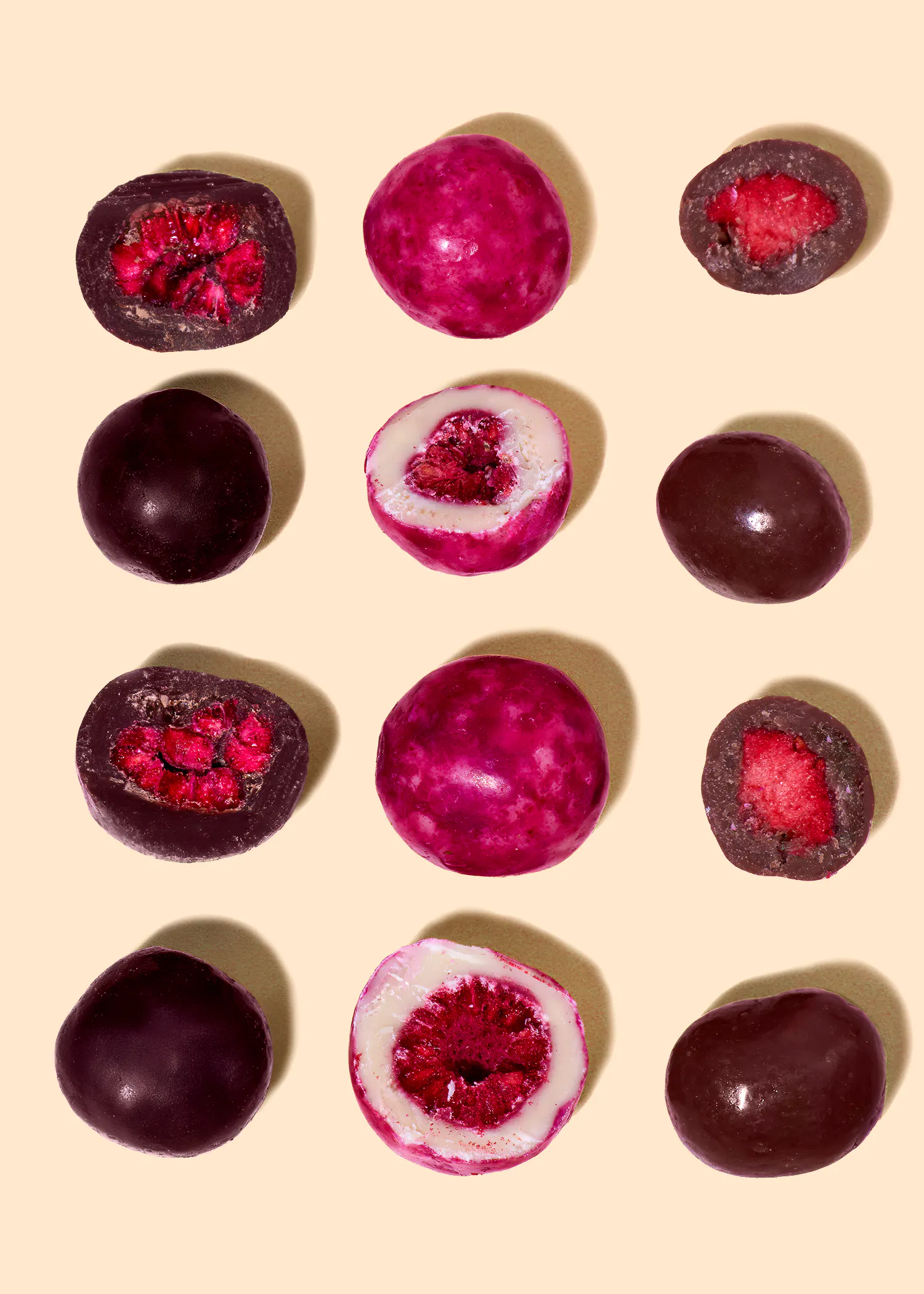 une grille de framboises enrobées de chocolat, certaines entières et d'autres coupées en deux, révélant leur intérieur rouge, avec des enrobages de chocolat noir, rose et blanc.
